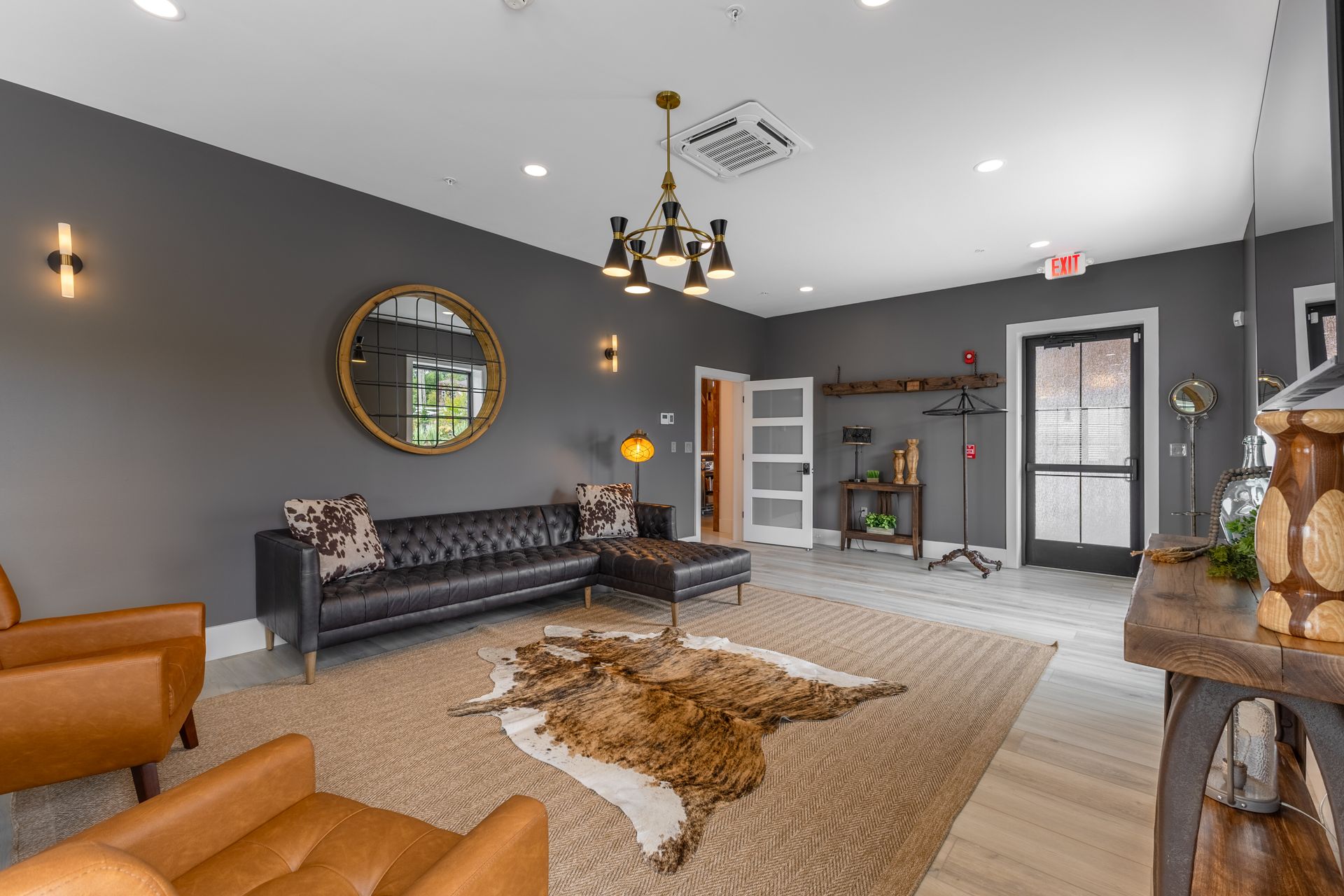 Stylish gray waiting room with black sofas, a chandelier, wall sconces, and a beige patterned rug