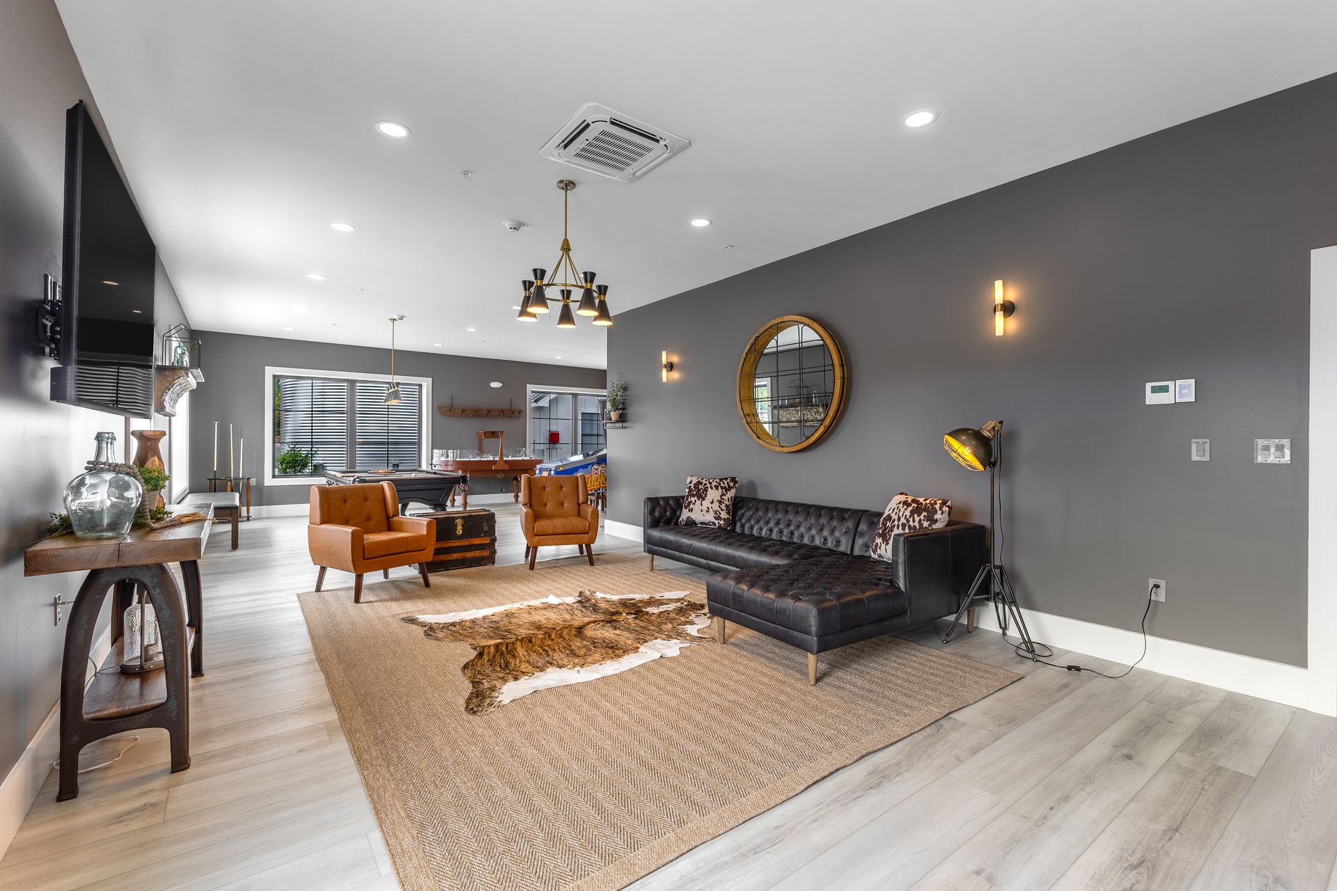 Modern living room with gray walls, black sofa, tan rug, and open dining area in the background