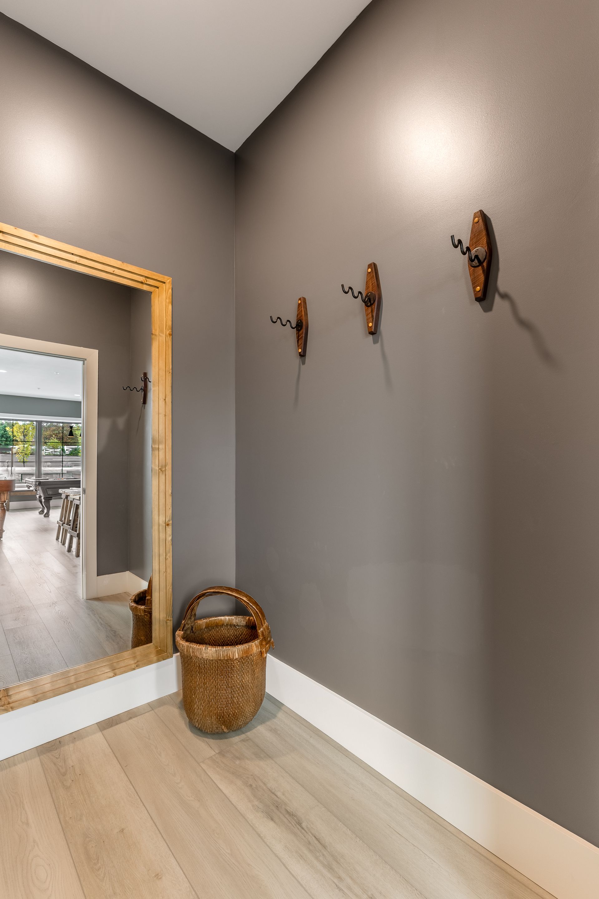 Hallway with gray walls, light wood floor, wicker basket, and wall-mounted coat hooks near a mirror