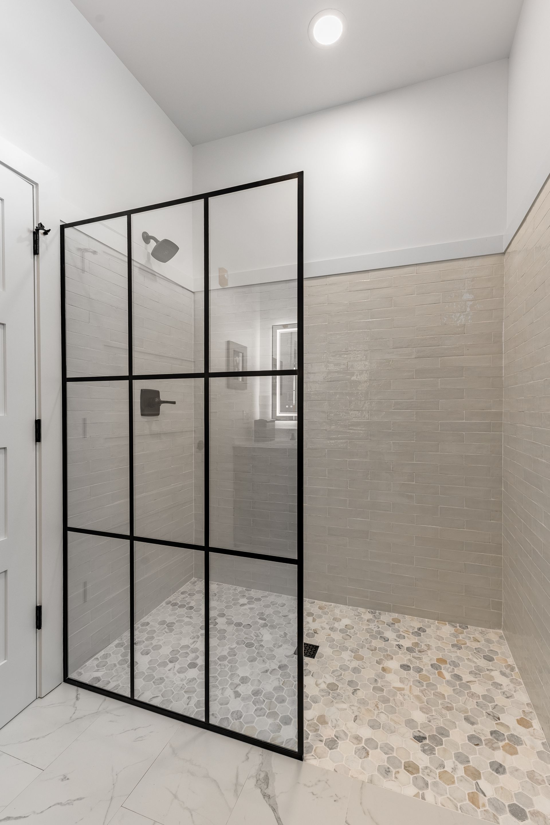 Modern bathroom with glass-enclosed shower, beige tile walls, and mosaic floor.
