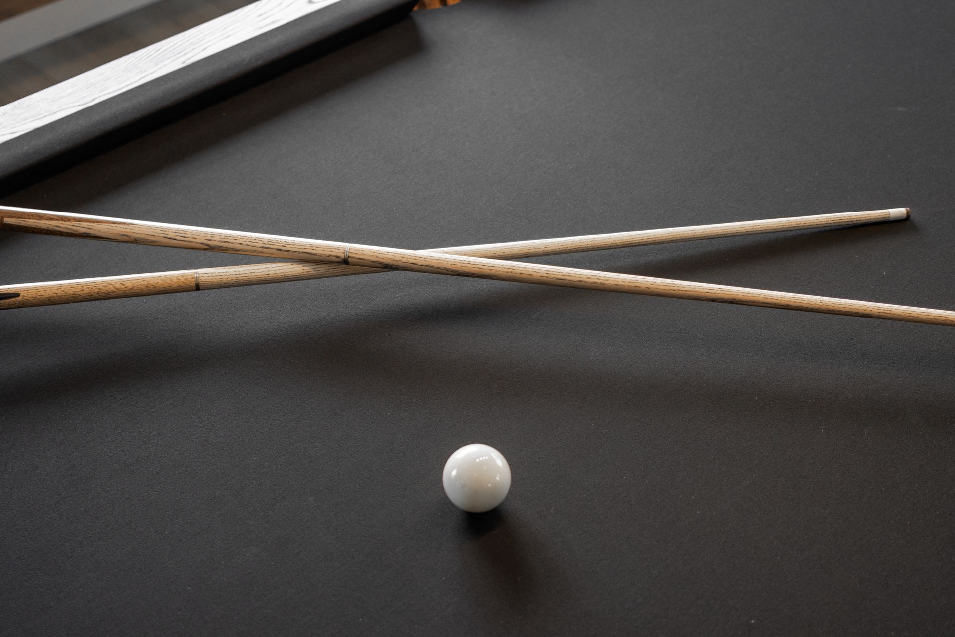 Two crossed pool cues on a dark table with a white billiard ball nearby