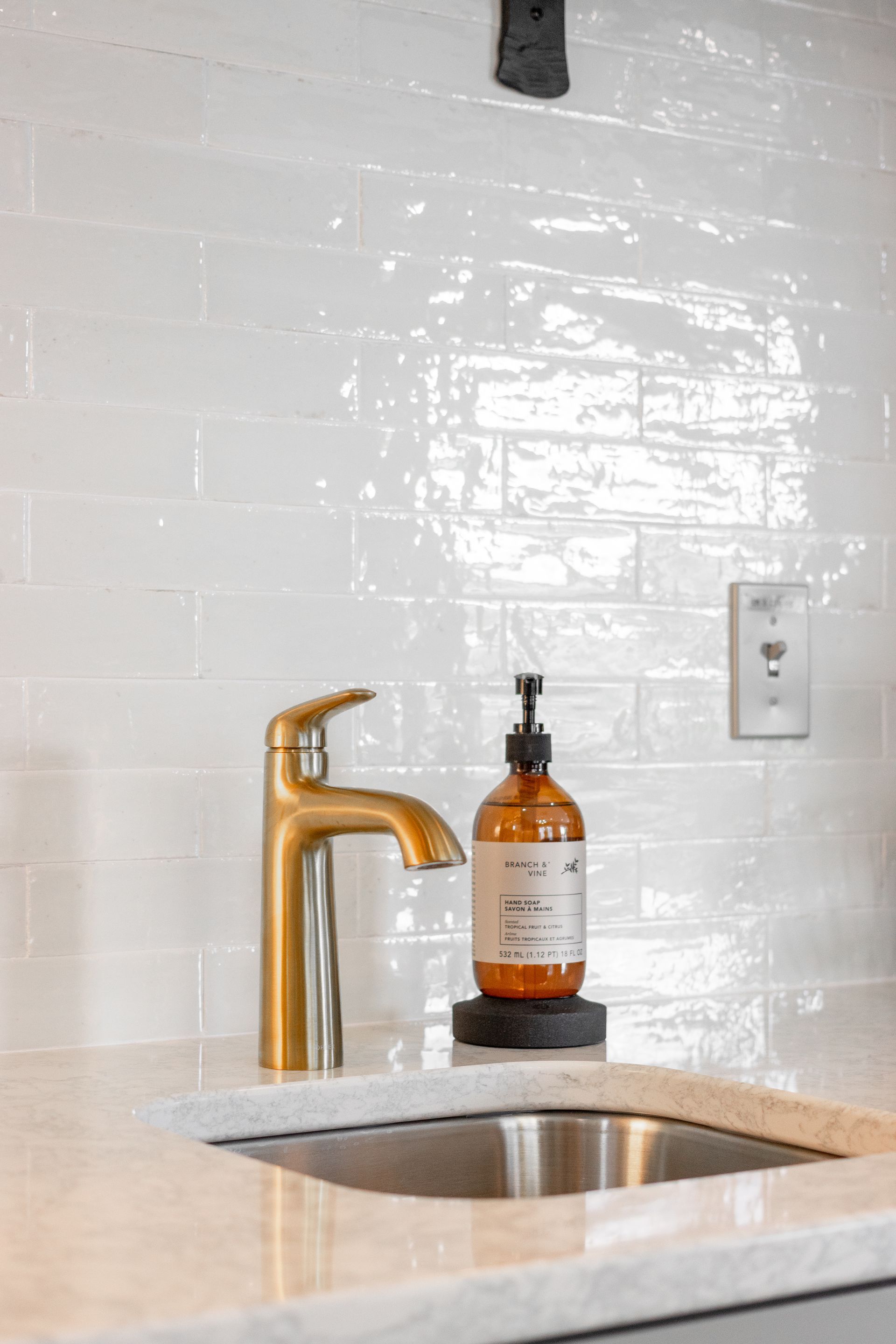 Kitchen sink with gold faucet, amber soap dispenser, and white tile backsplash
