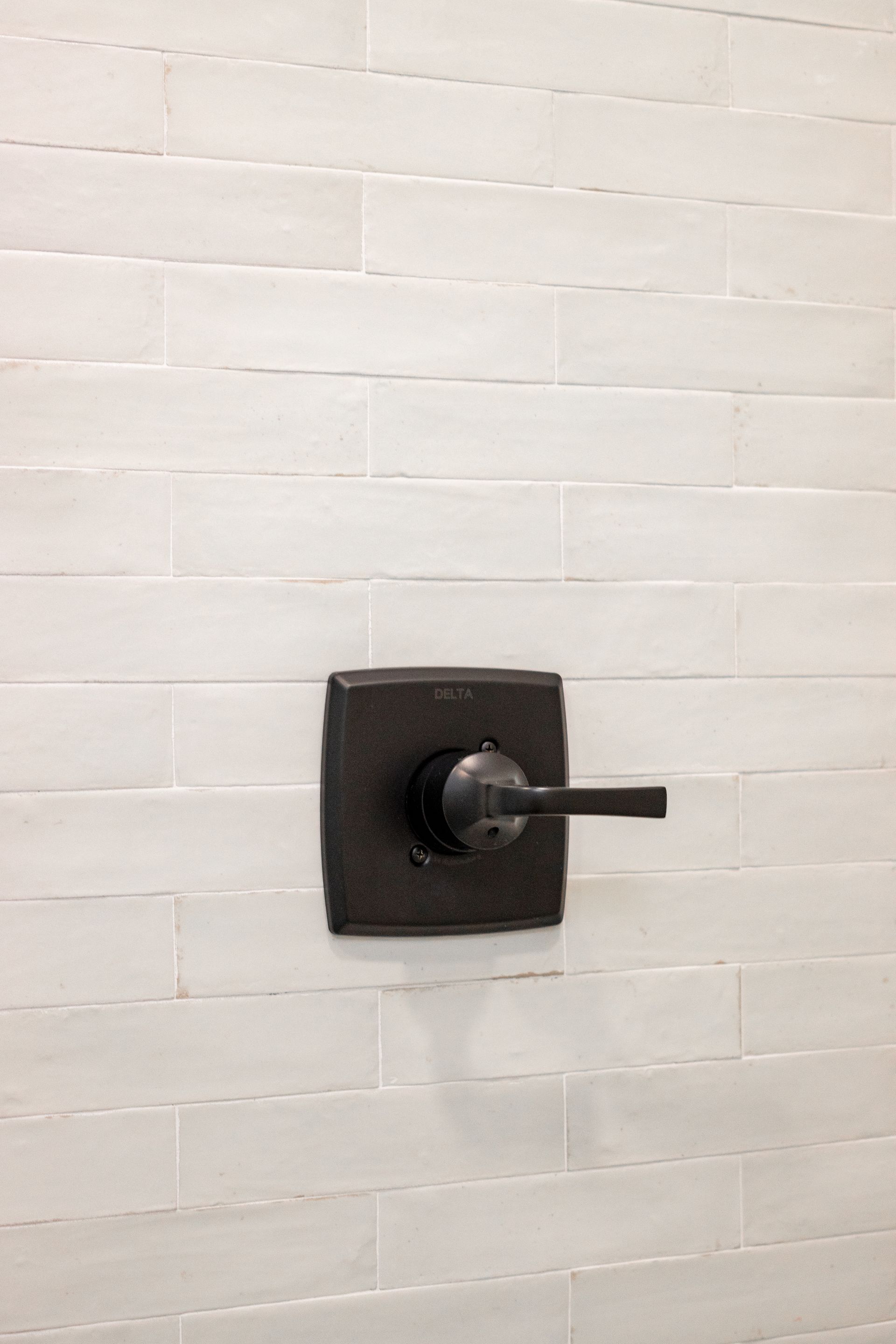 Black wall-mounted handle or lever on a white tiled wall.
