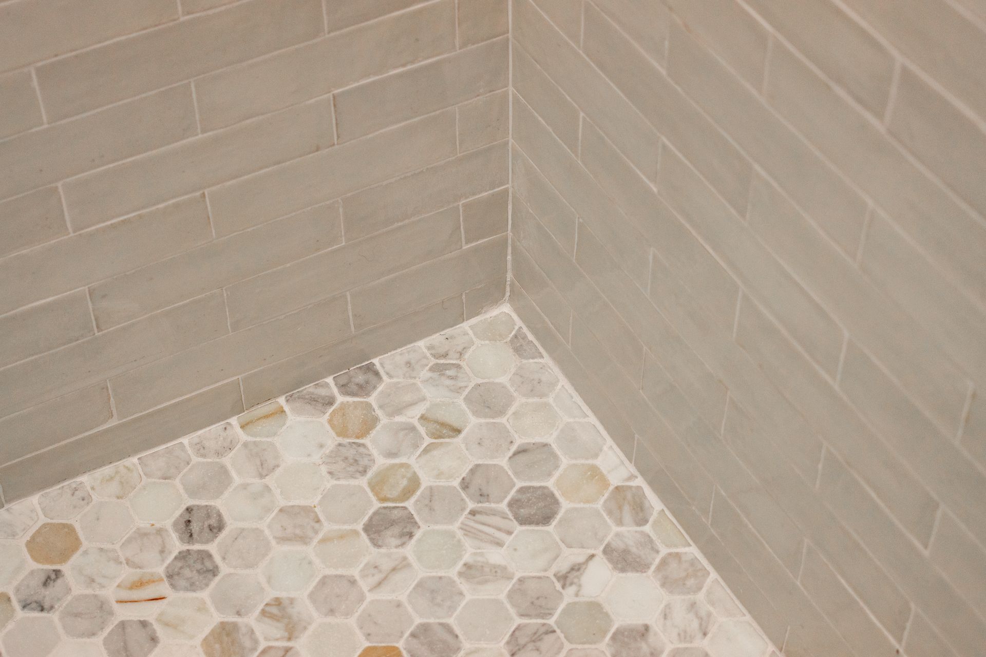Corner of a tiled shower with beige walls and a multicolored hexagon tile floor