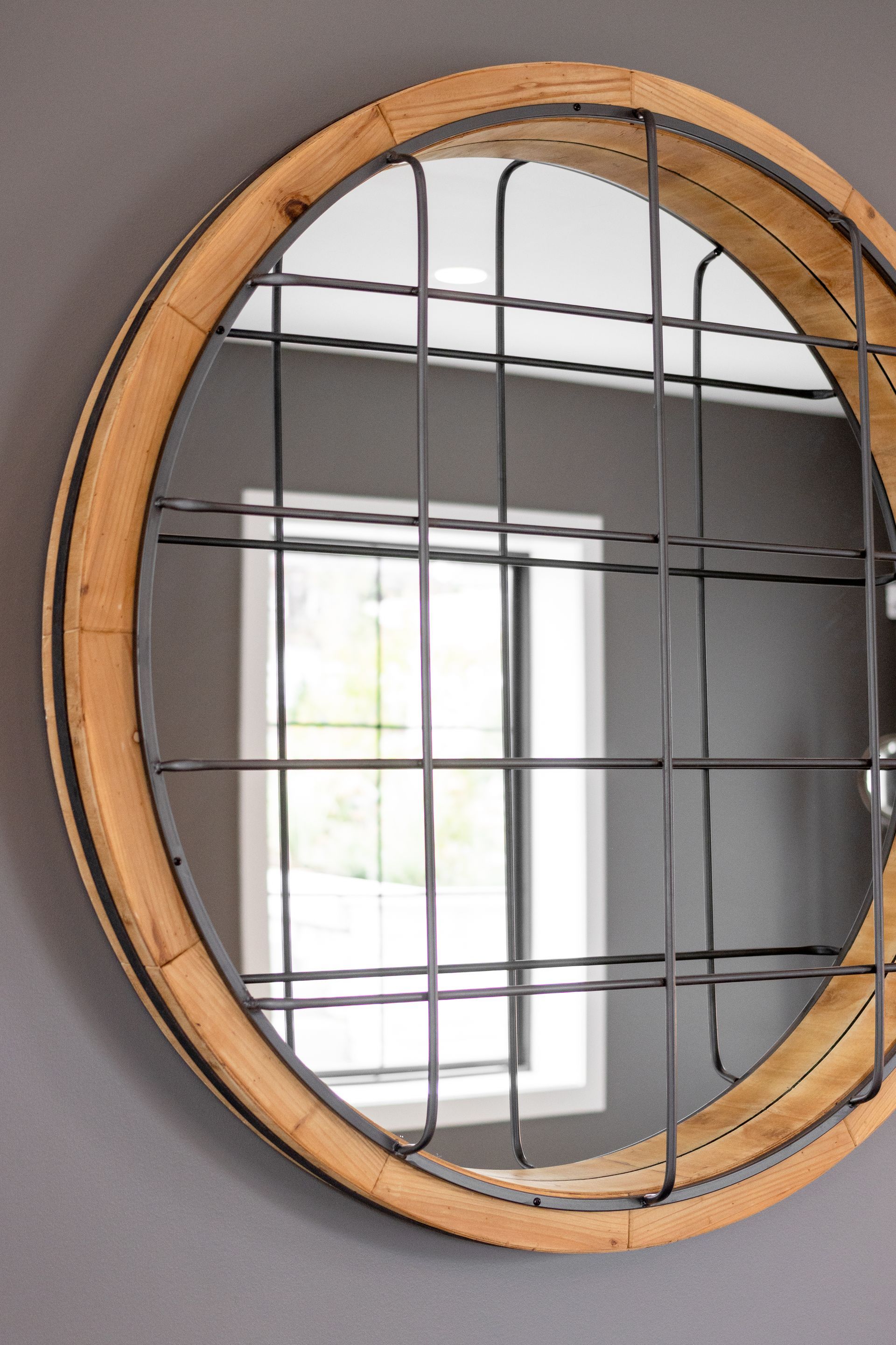 Round wooden-framed mirror reflecting a bright window in a room