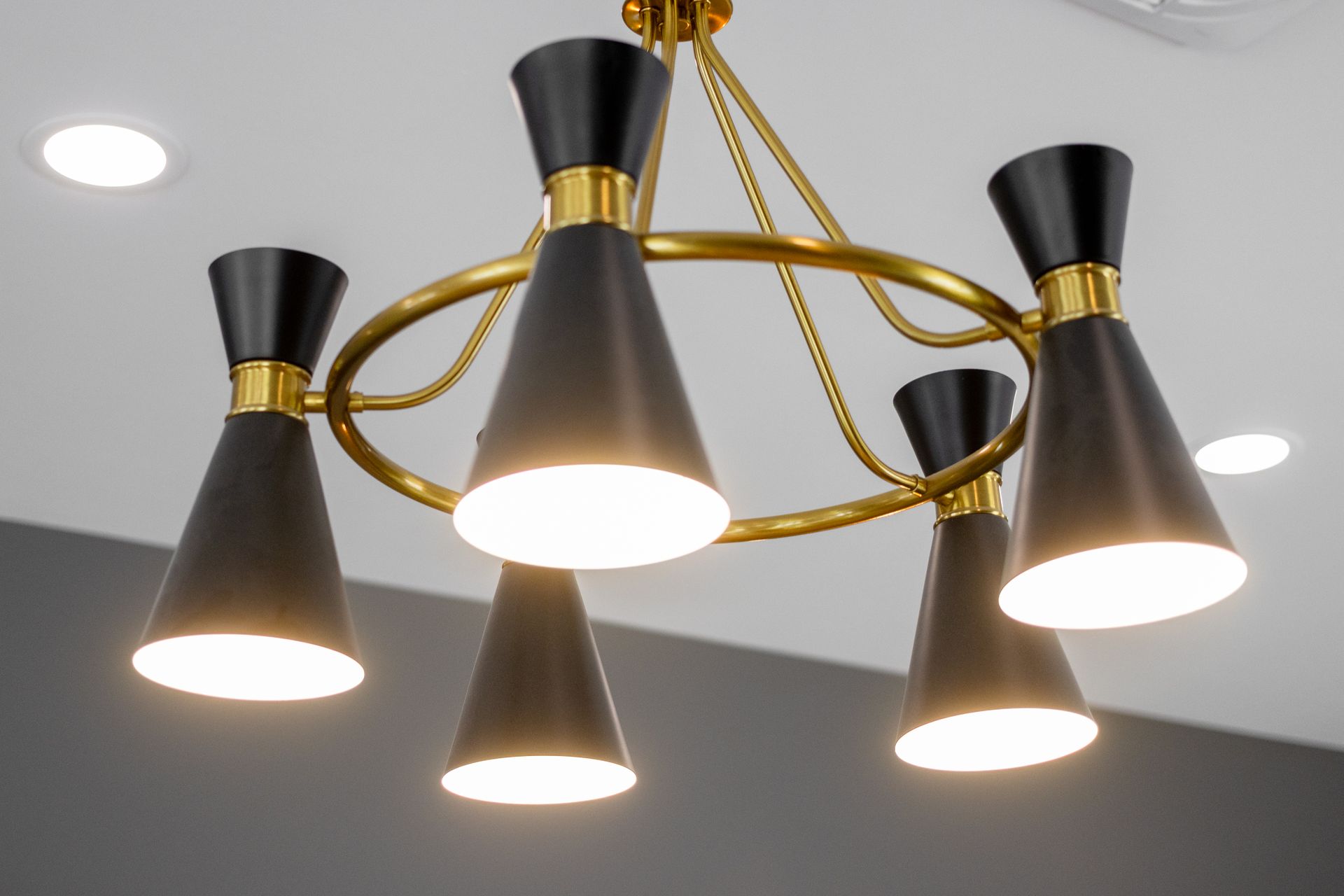 Modern gold and black chandelier with five lit cone-shaped shades on a white ceiling