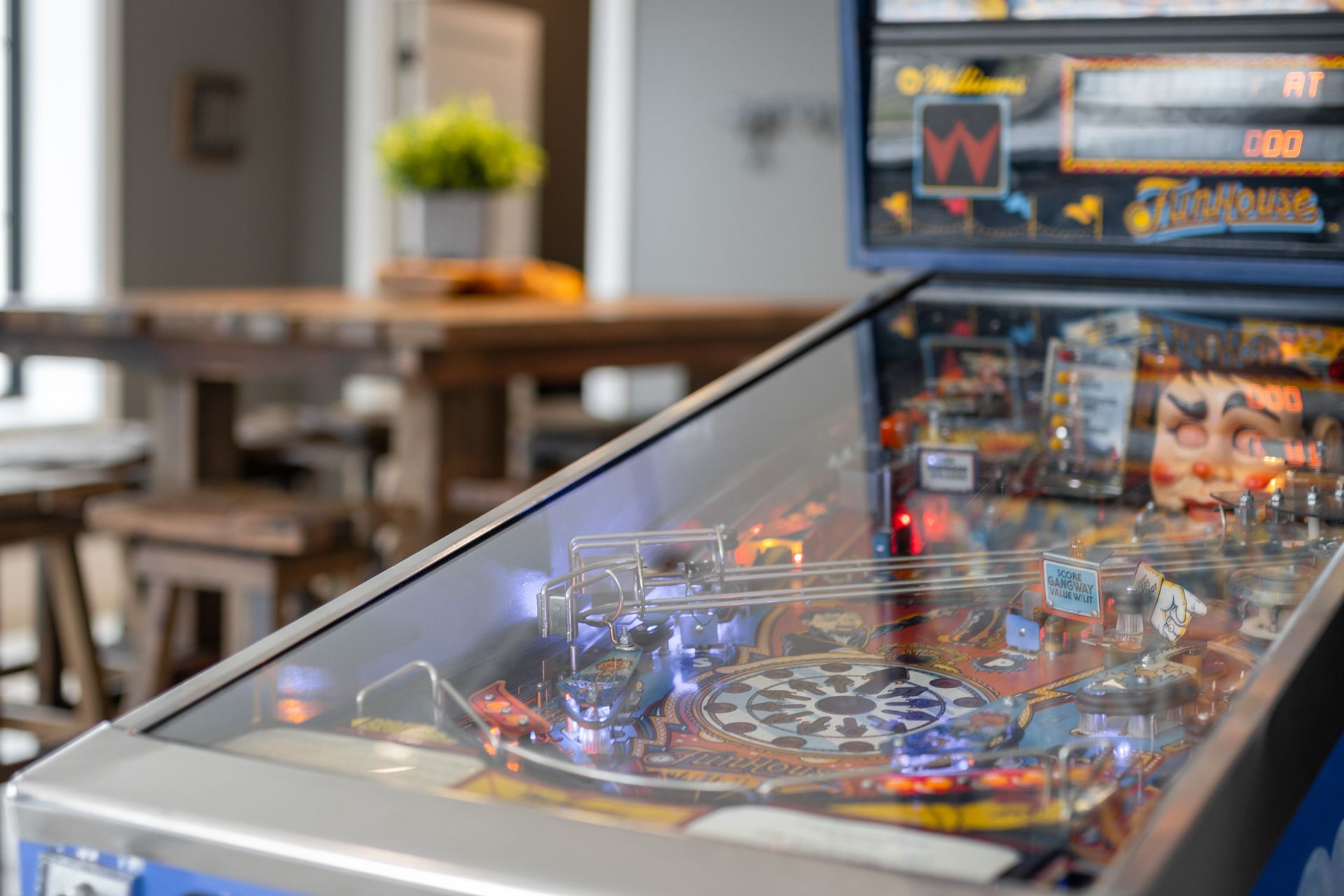 Pinball machine with colorful lights in a modern room, with tables and chairs in the background