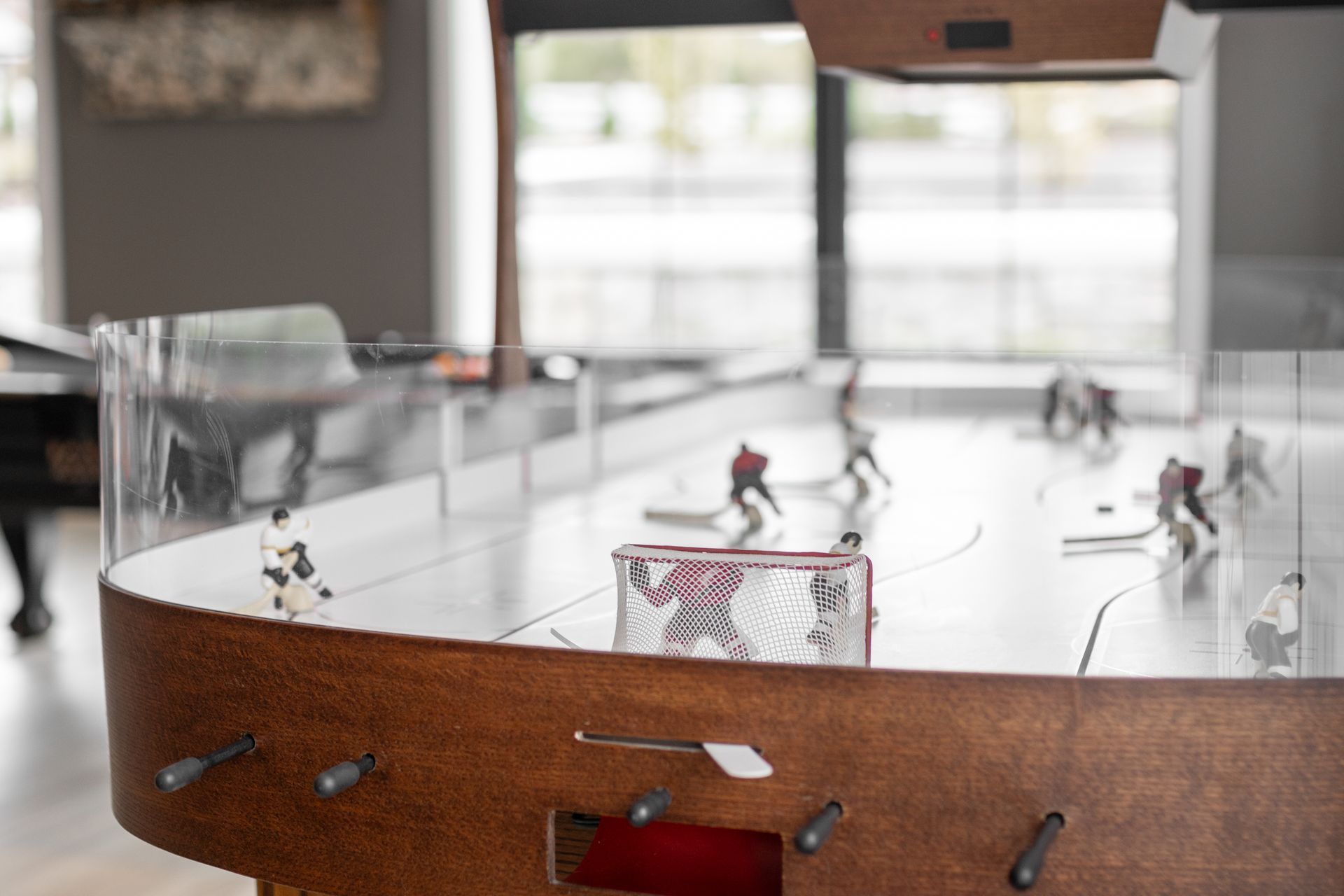 Mini tabletop hockey rink with players and a red goal, indoors by a window
