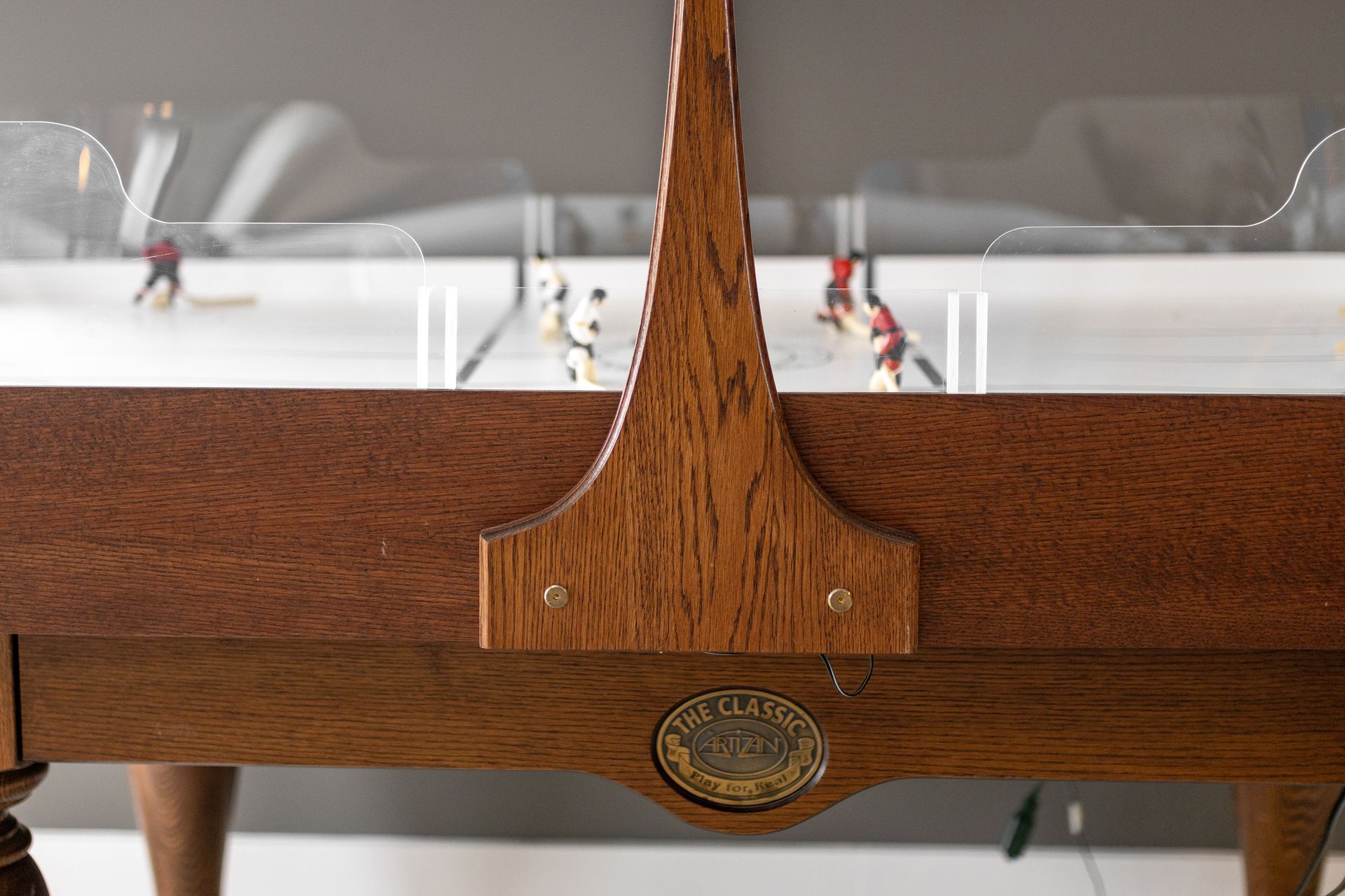 Wooden dining table with a carved center support, seen in front of white chairs and a set table.