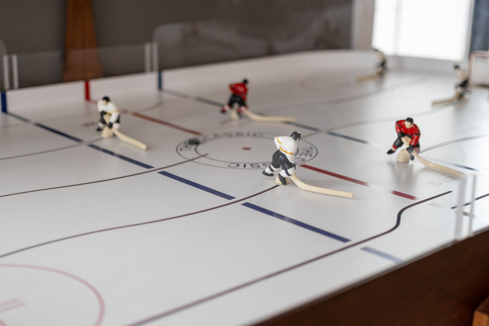 Miniature hockey players on an indoor tabletop rink, with red and white figures chasing the puck.
