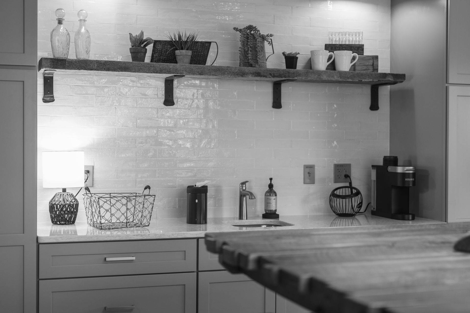 Black-and-white kitchen with shelves, jars, bottles, cabinets, and a wooden table in the foreground