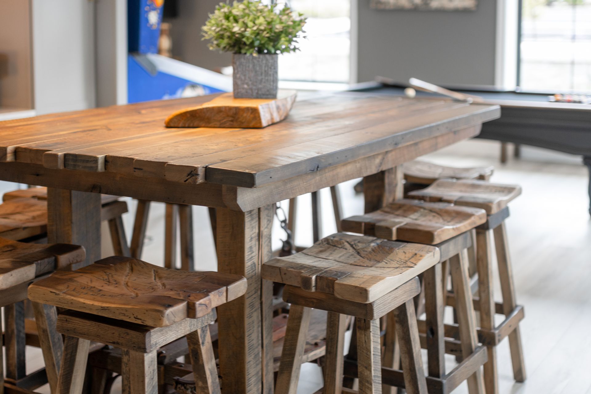 Rustic wooden dining table with matching stools in a bright modern room, topped with a small potted plant