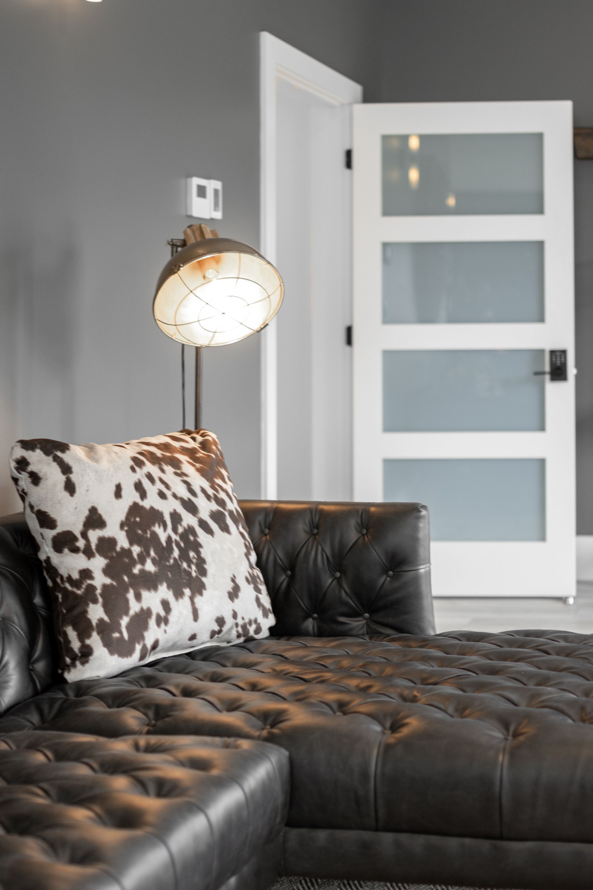 Modern living room with a black tufted sectional, patterned pillow, floor lamp, and white glass-panel door