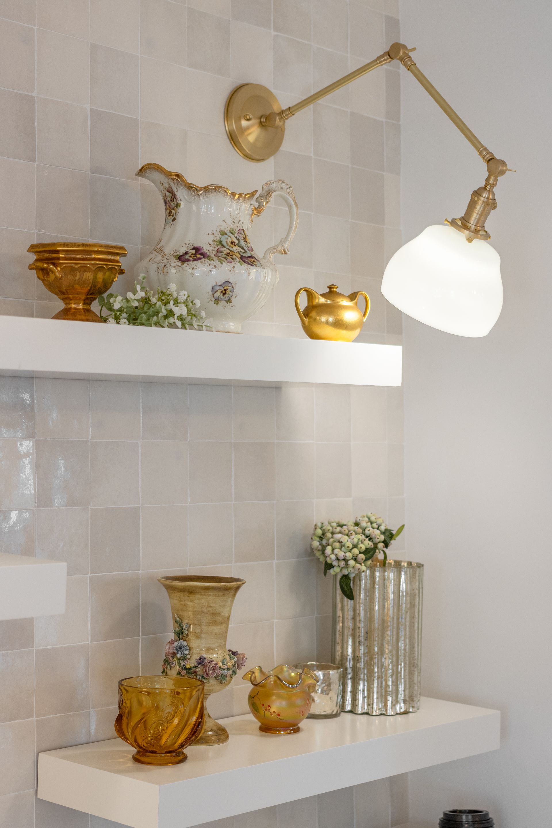 Gold and white decorative vases and bowls displayed on floating shelves beside a brass wall lamp.