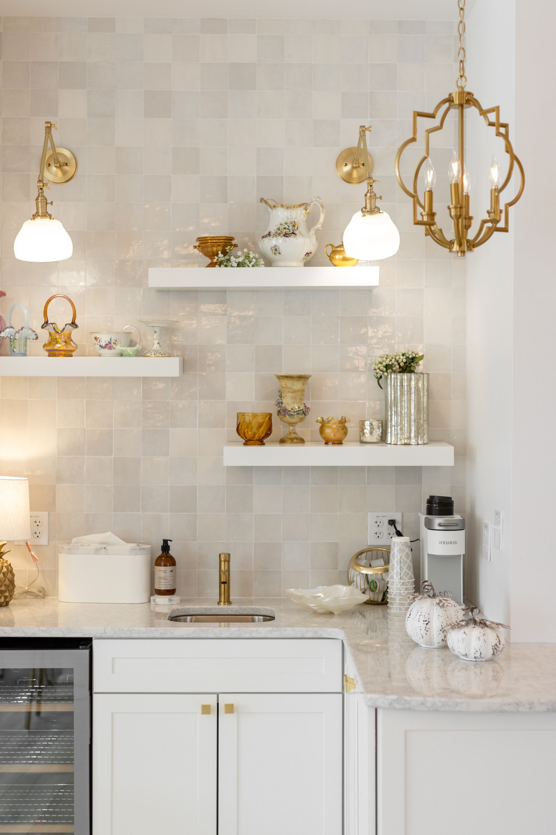 Bright white kitchen with gold accents, floating shelves, and a marble countertop holding small decor and appliances