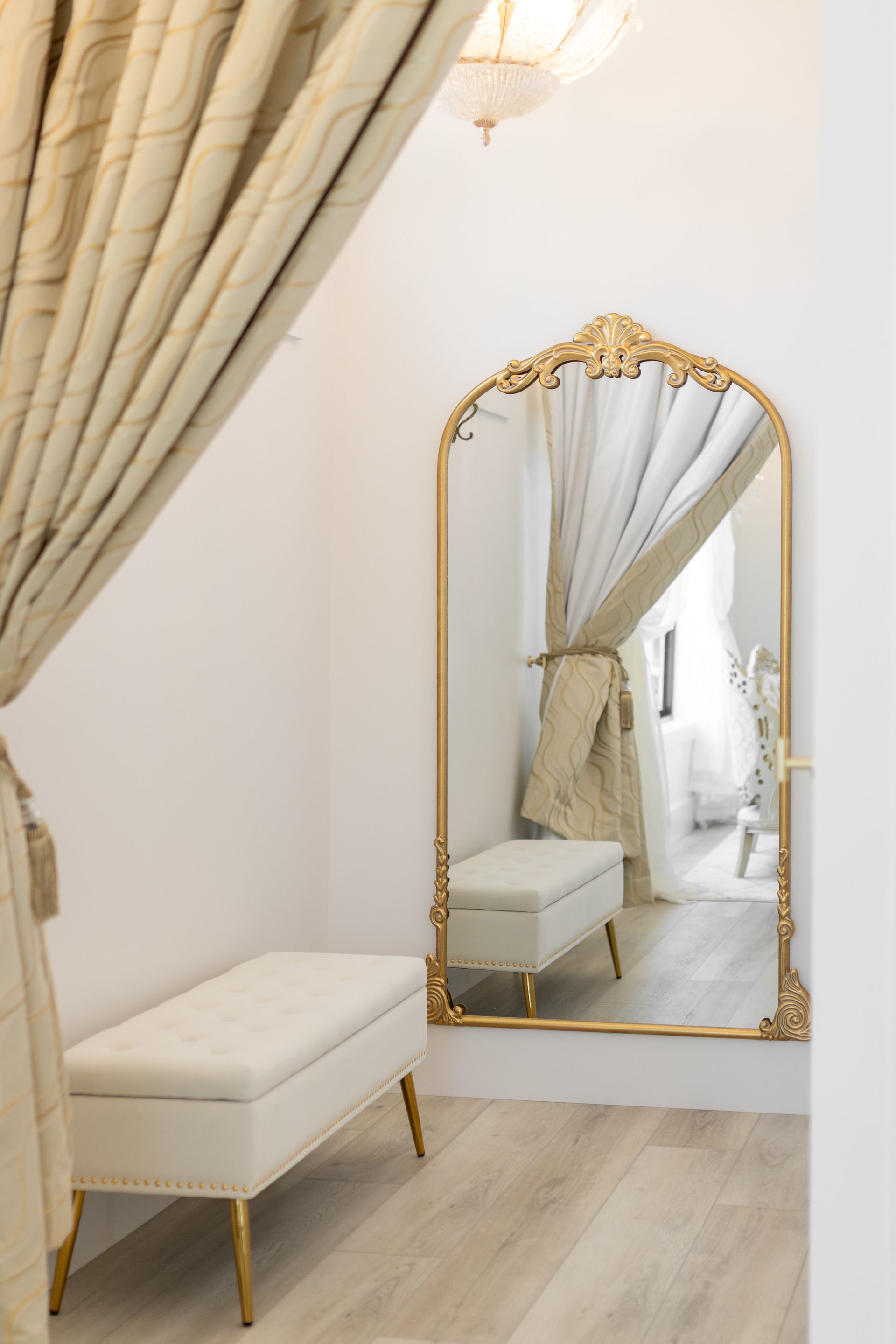 Elegant dressing room with gold-framed mirror, cream bench, and draped curtains in a soft beige interior