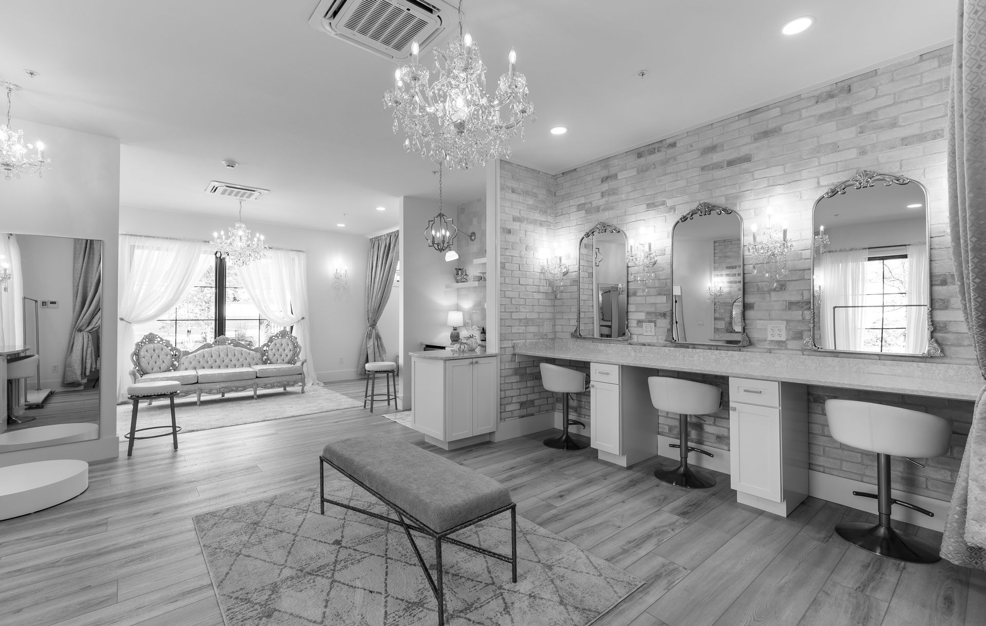 Bright modern salon with styling stations, mirrors, chairs, and a chandelier over wood flooring.