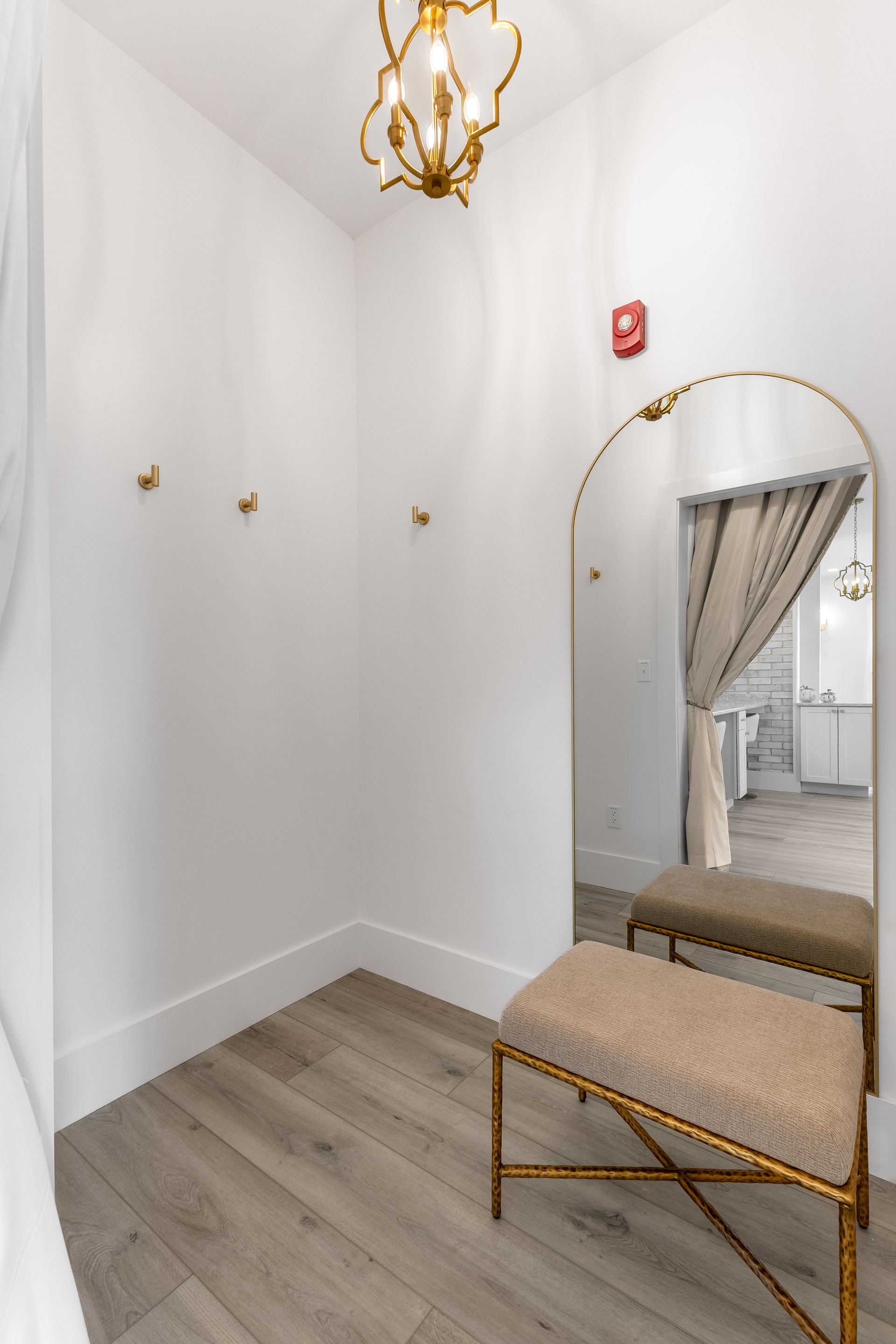Small stylish dressing room with arched mirror, bench, white walls, wood floor, and gold accents