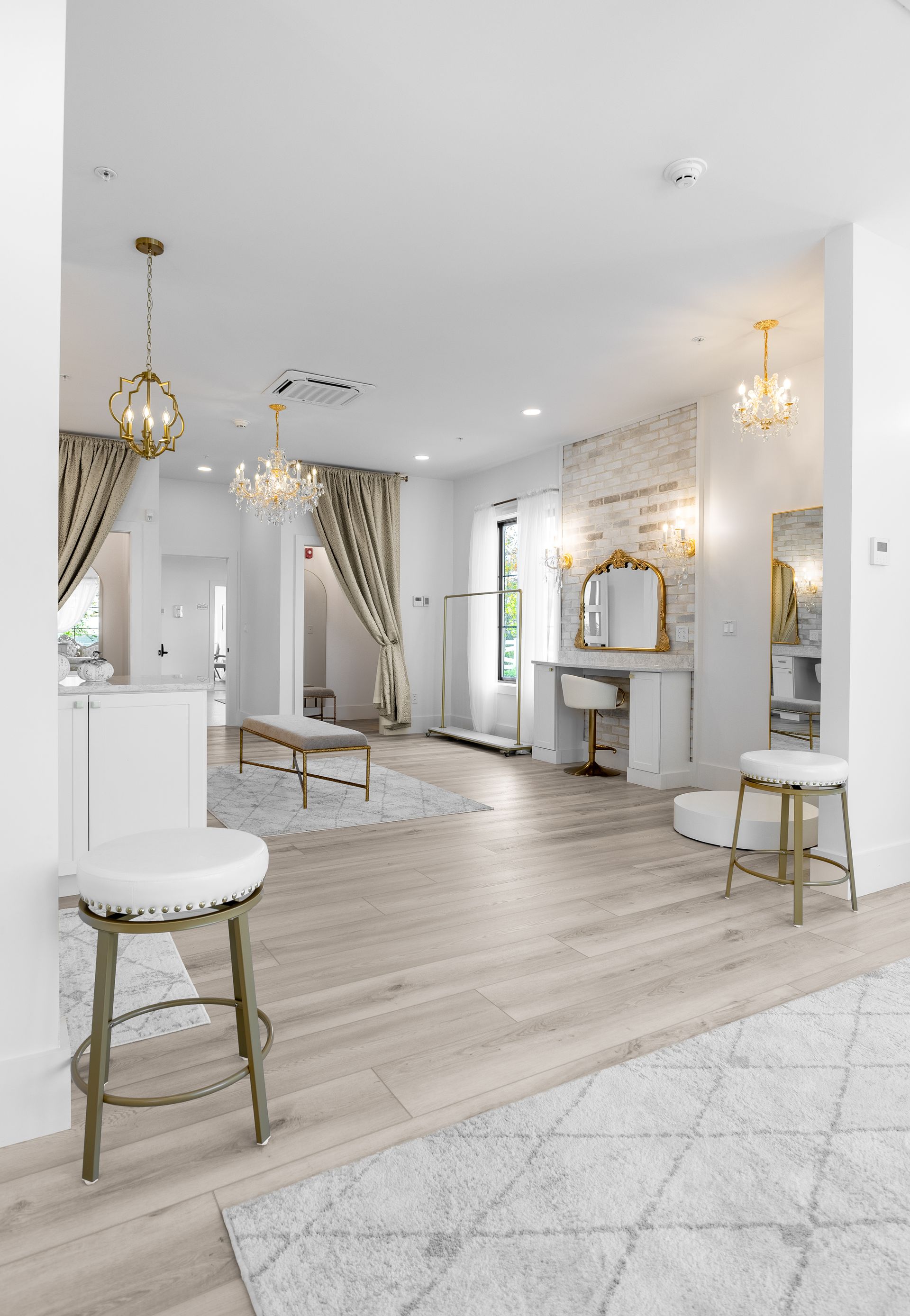 Bright white salon interior with mirrors, gold accents, curtains, and chairs on a light wood floor.