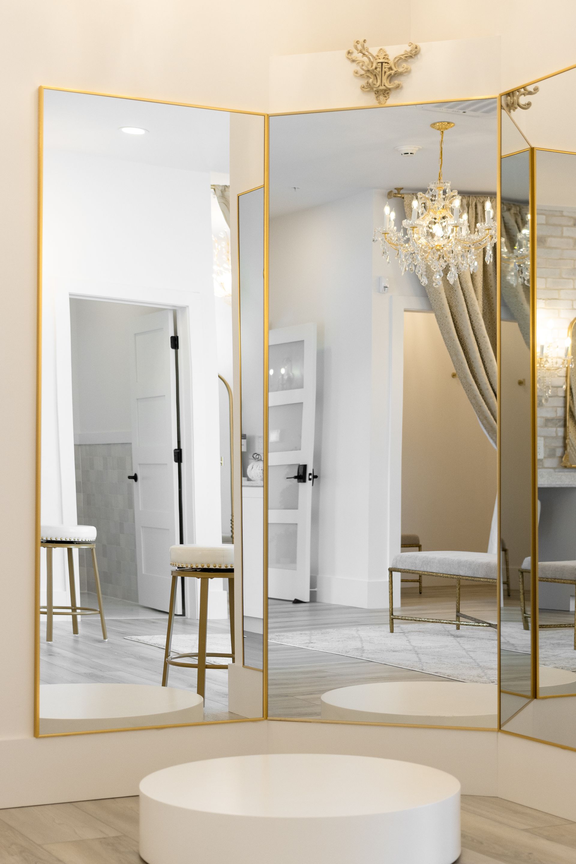 Gold-framed floor mirror in a bright room with draped curtains and a round white tub in front