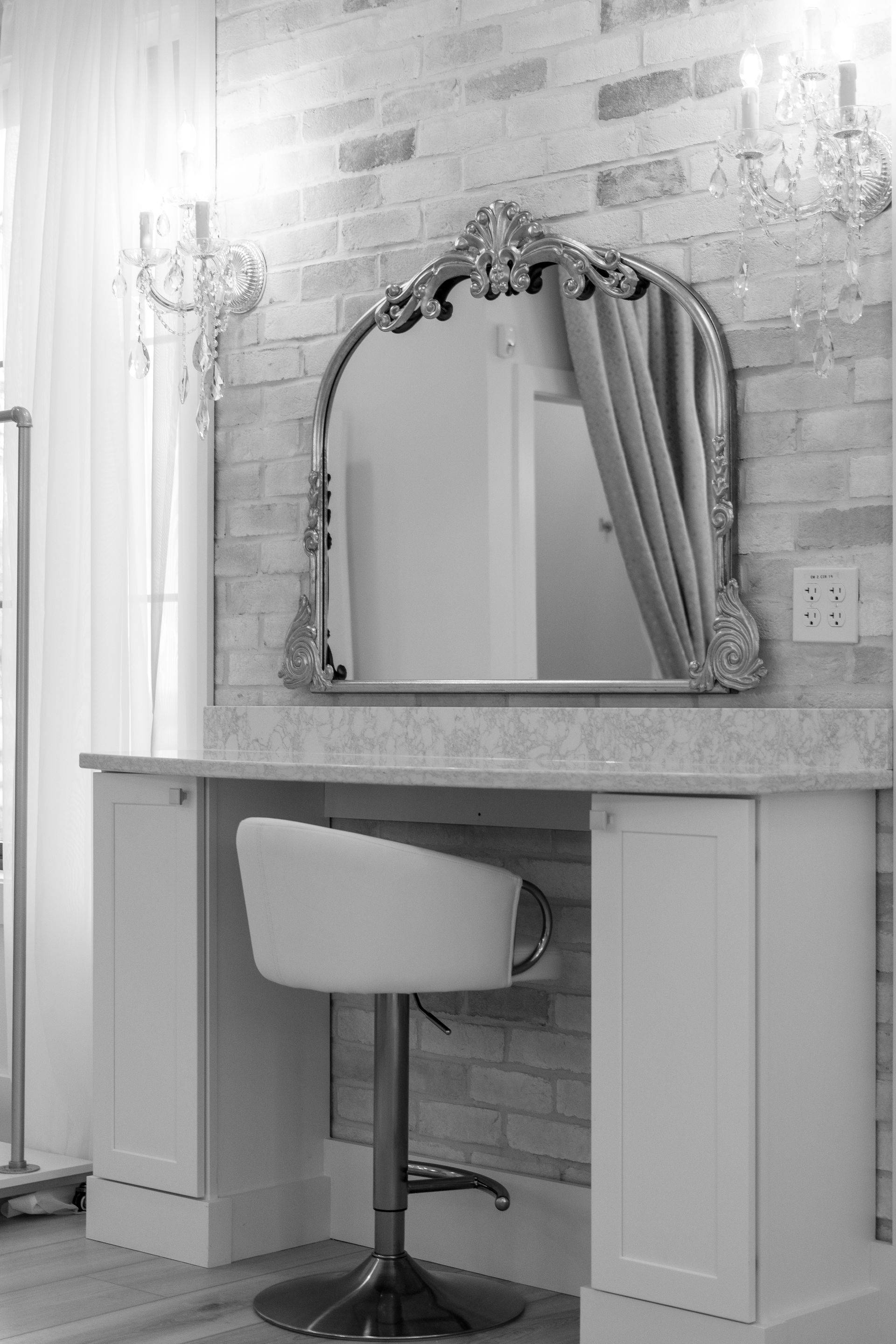 Vanity table with ornate mirror, stool, and curtains in a bright room