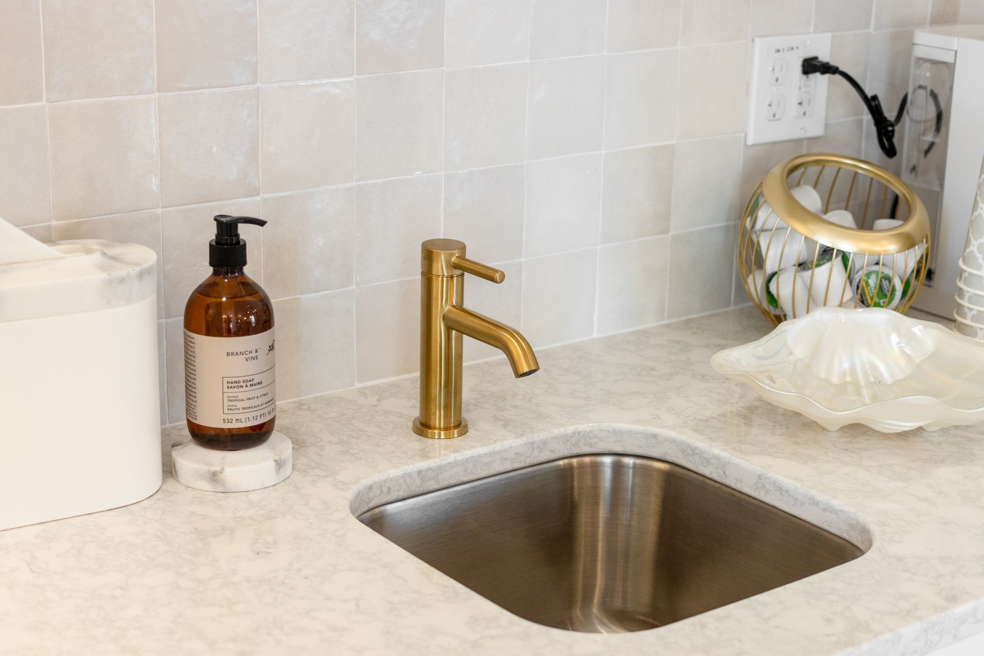 Kitchen sink with gold faucet, soap dispenser, and decorative bowl on a light countertop.