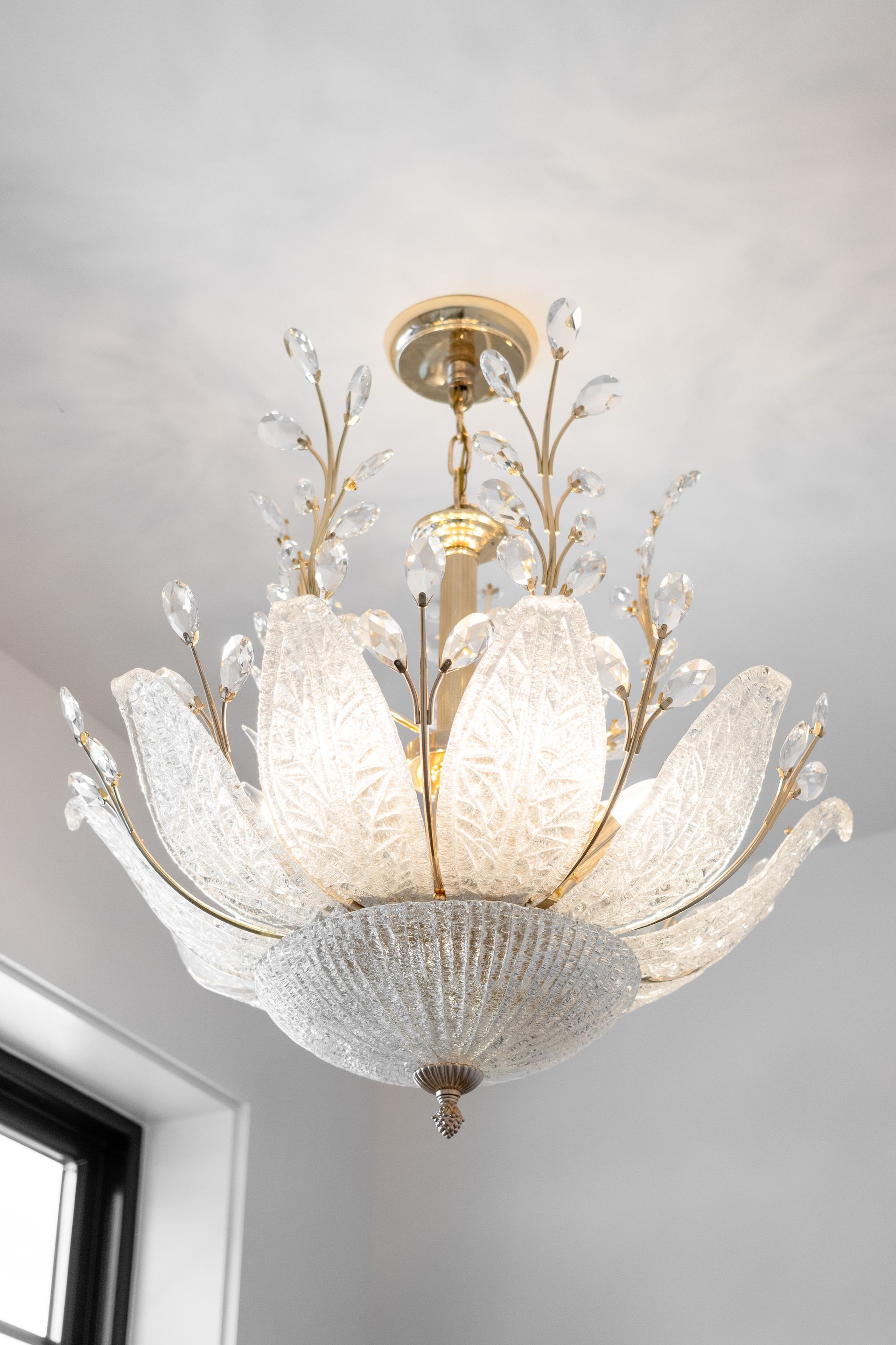 Ornate gold and white chandelier with crystal petals hanging from a ceiling