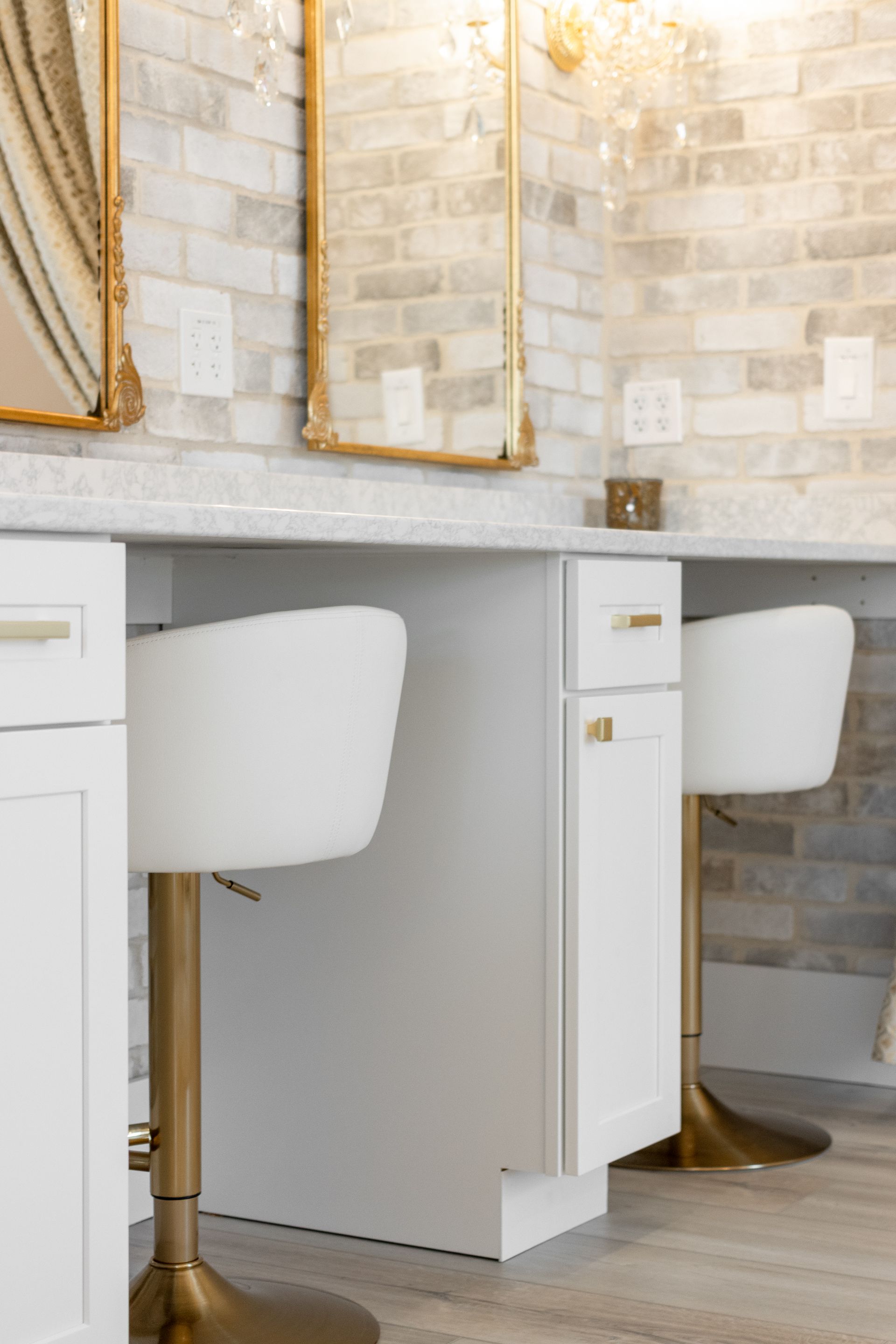 Modern bathroom vanity with white cabinets, gold-framed mirrors, and light brick tile walls.