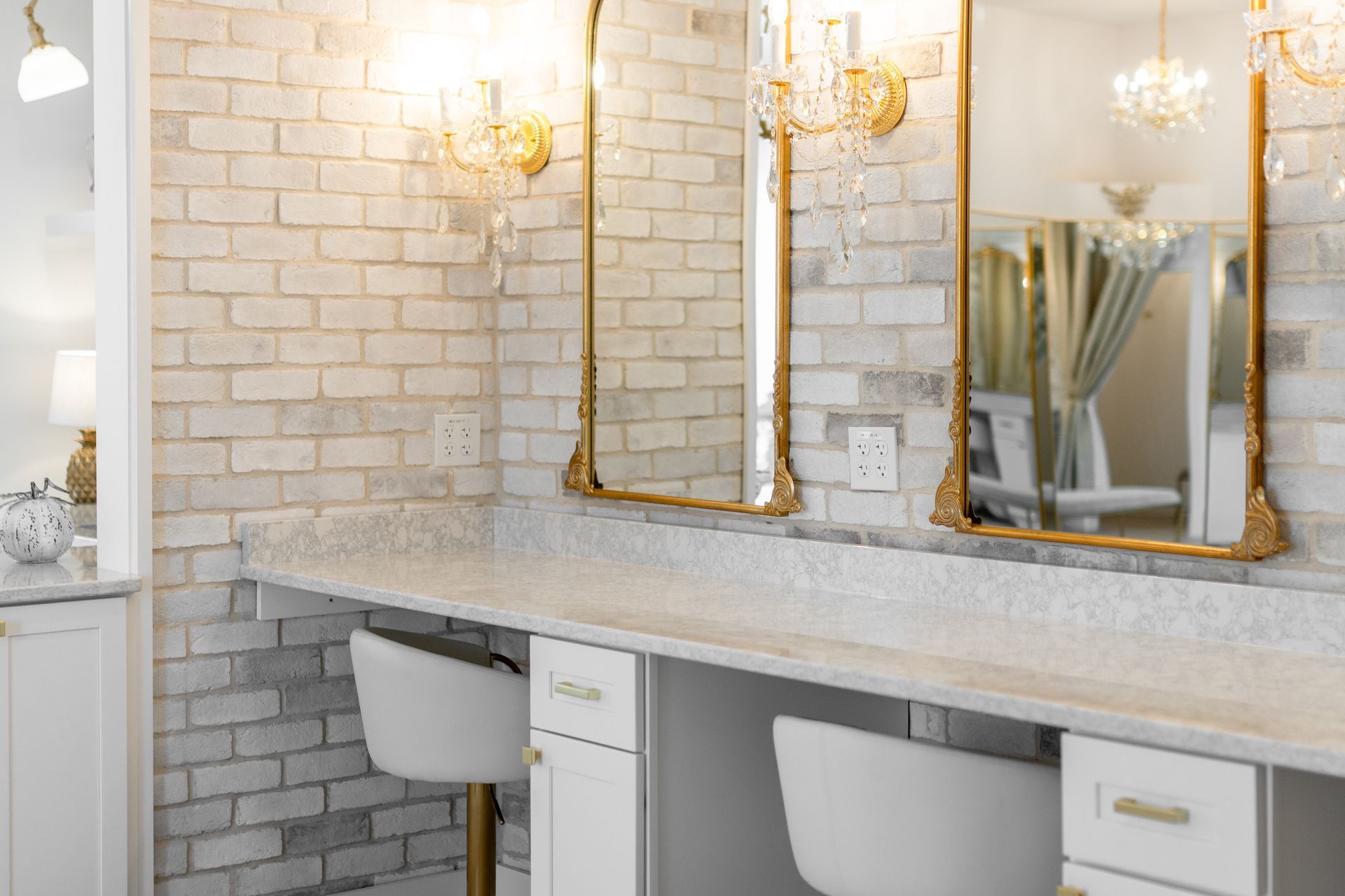 Modern bathroom vanity with double sinks, gold-framed mirrors, wall sconces, and white brick walls