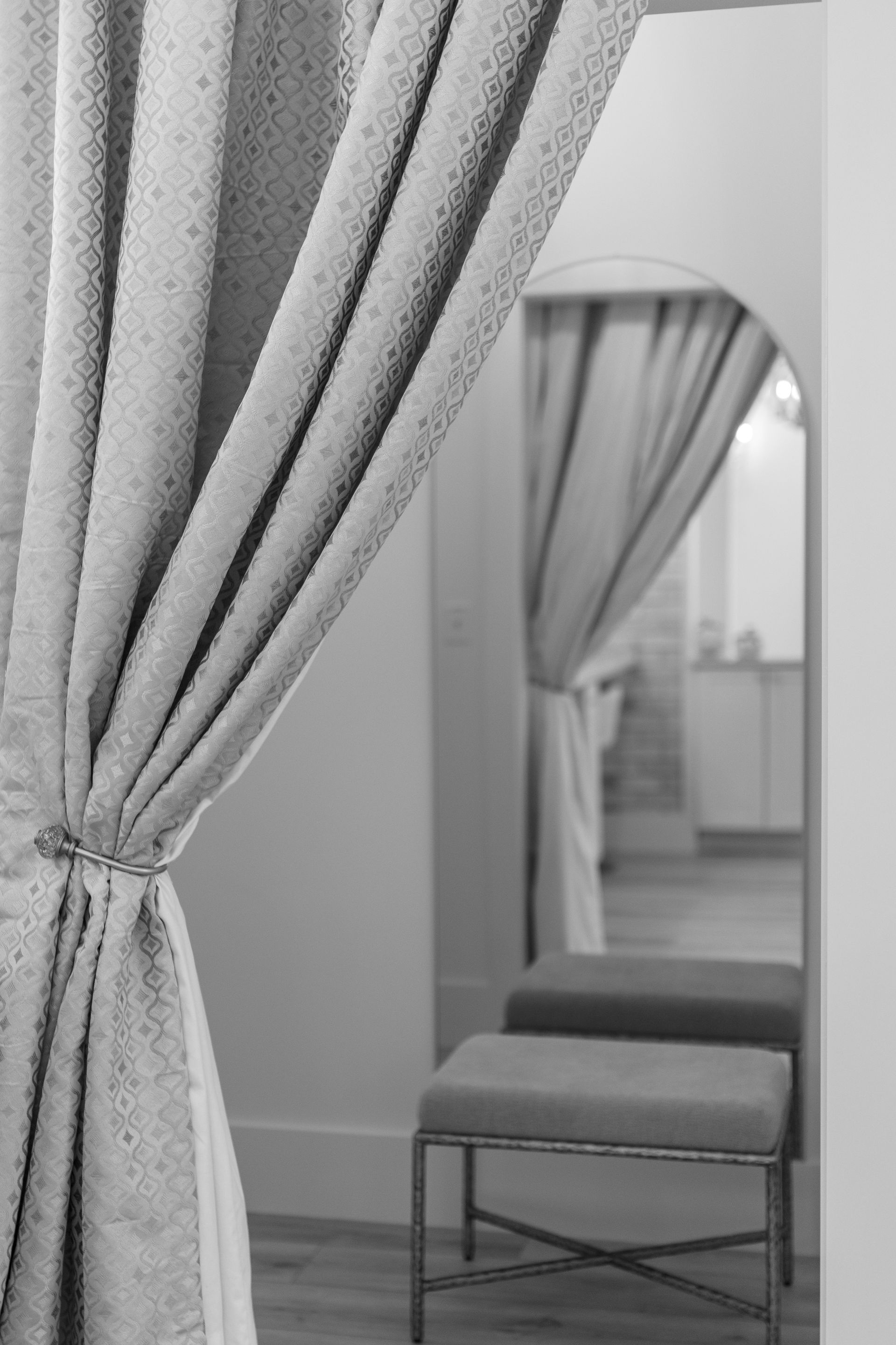 Curtain-tied dressing room with bench and mirror reflecting a window and draped curtain