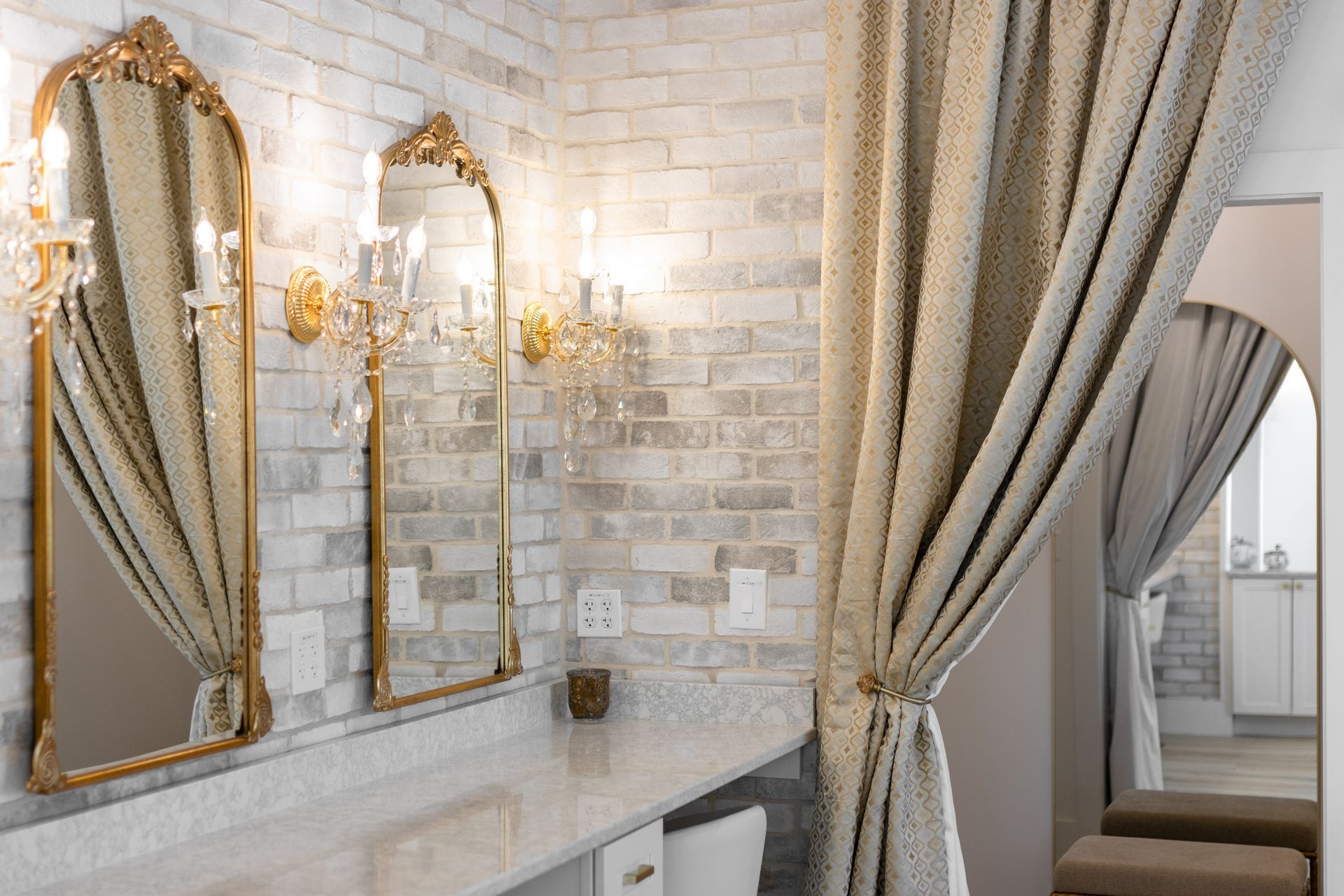Elegant vanity corner with gold-framed mirrors, wall sconces, and a draped curtain beside a marble counter