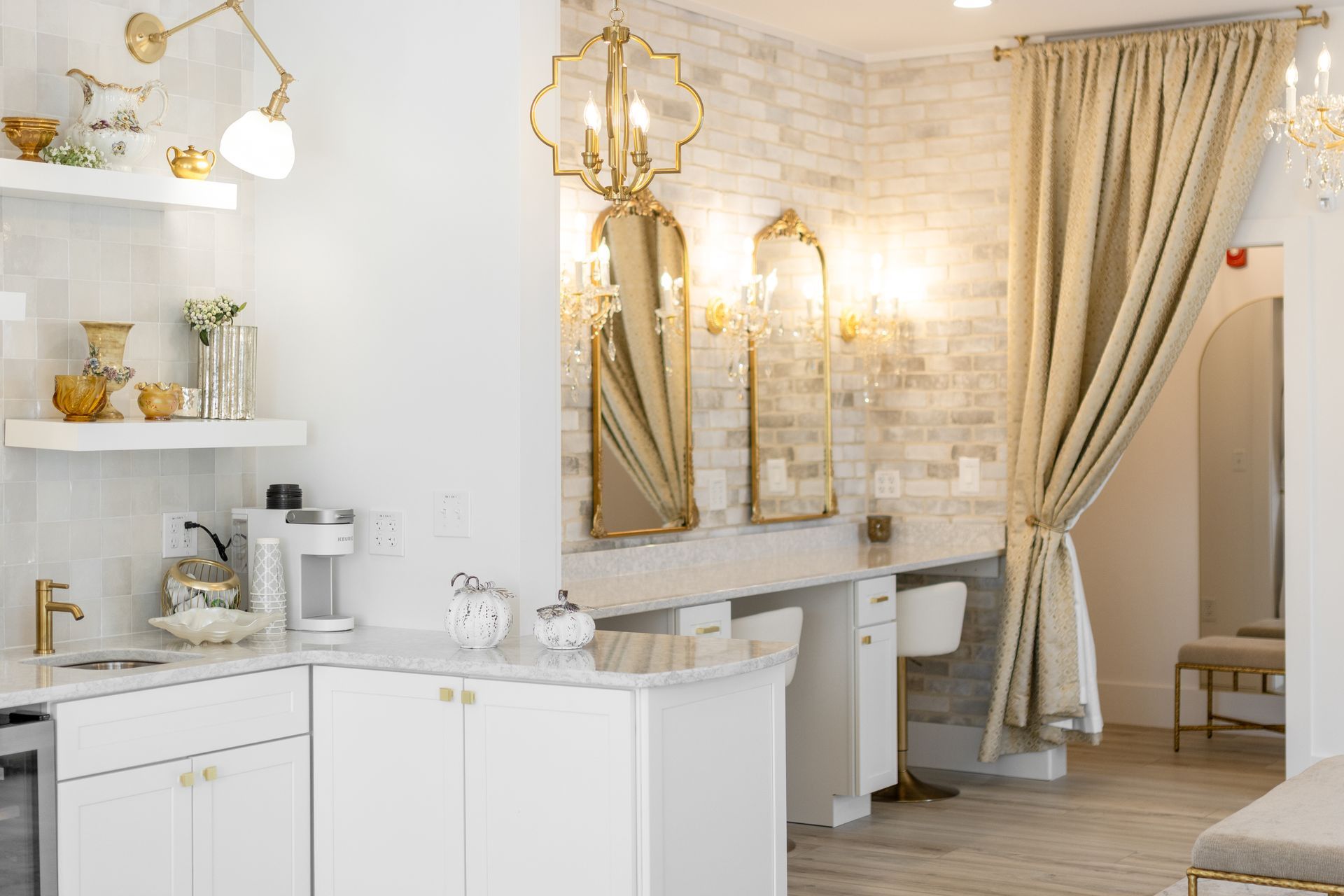 Elegant white and gold kitchen with marble counters, open shelves, and ornate curtains by a doorway