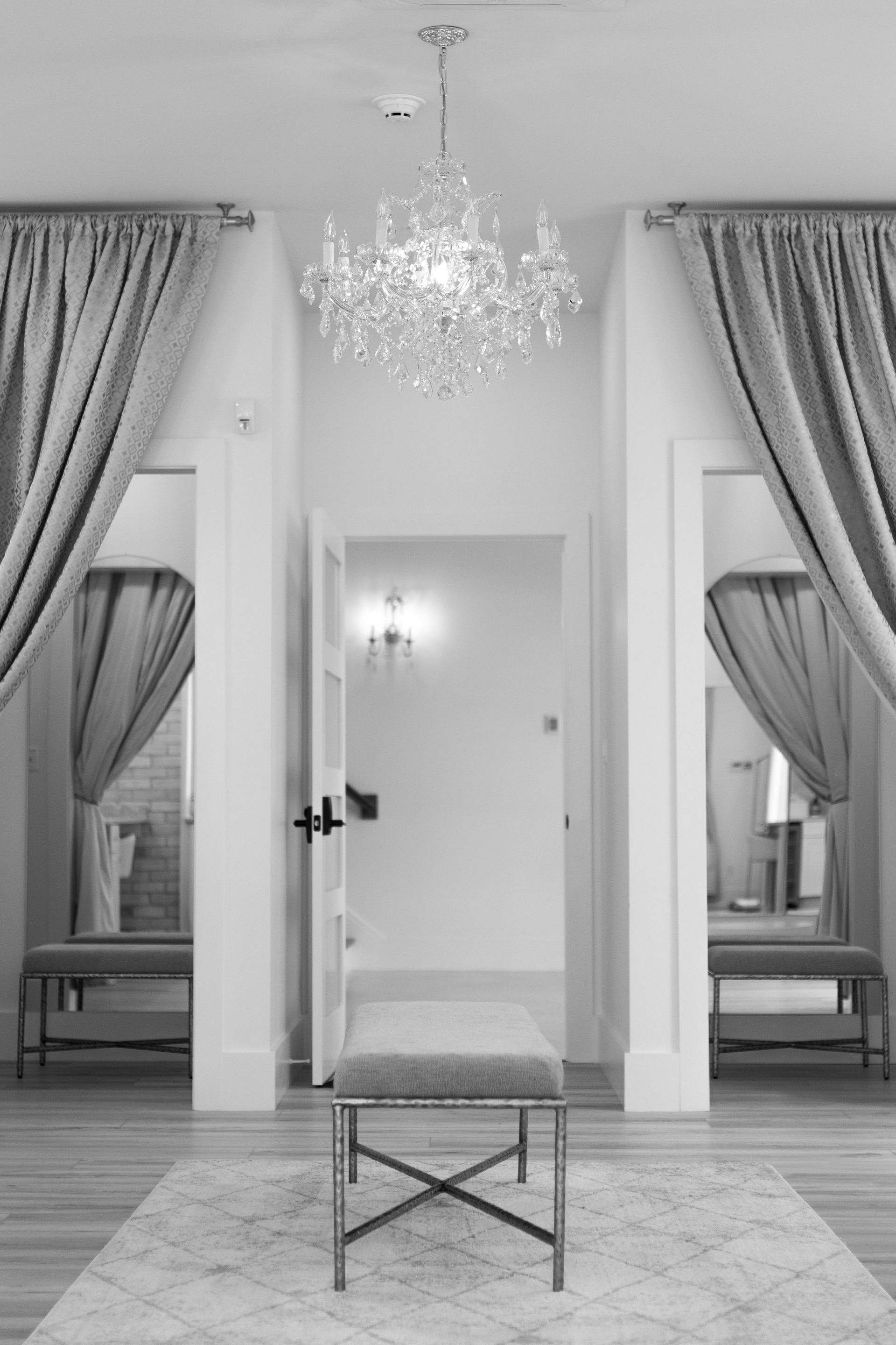 Elegant dressing room with crystal chandelier, draped mirrors, and a small bench on a patterned rug.