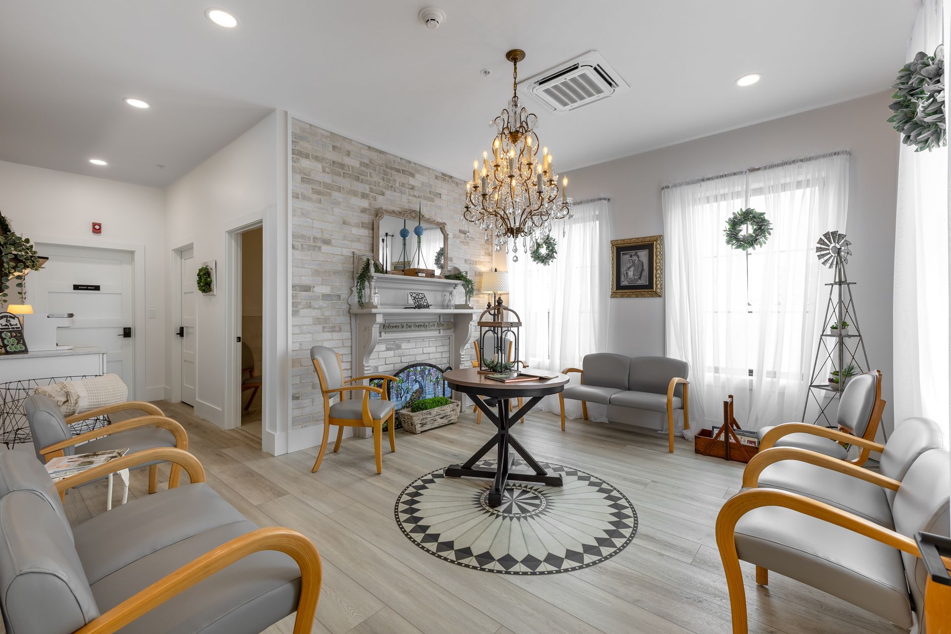 Bright waiting room with white walls, chandeliers, and gold-trimmed chairs around a central table.