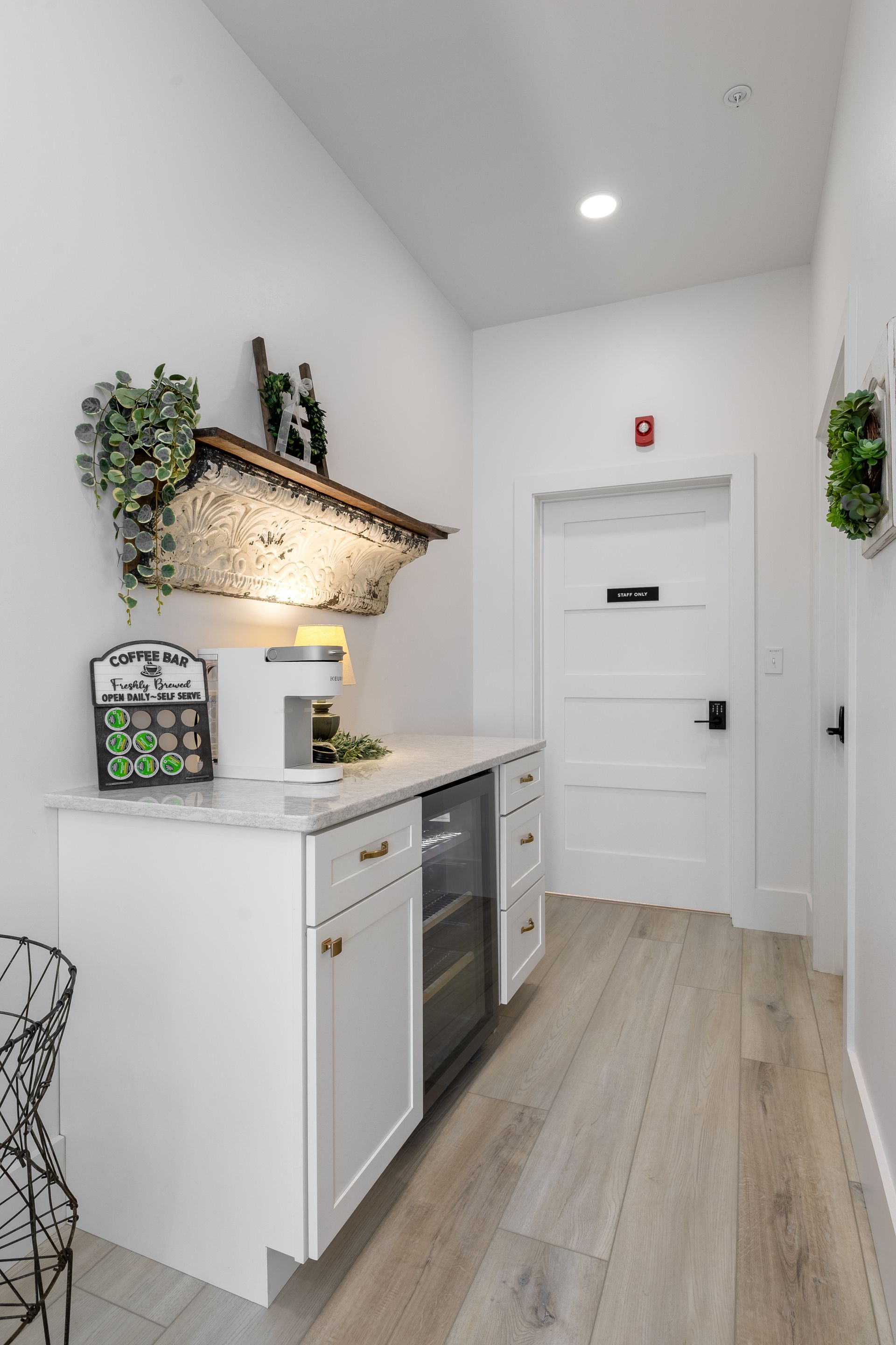 Bright narrow hallway with white cabinets, wood floor, wall shelves, and a white door at the end
