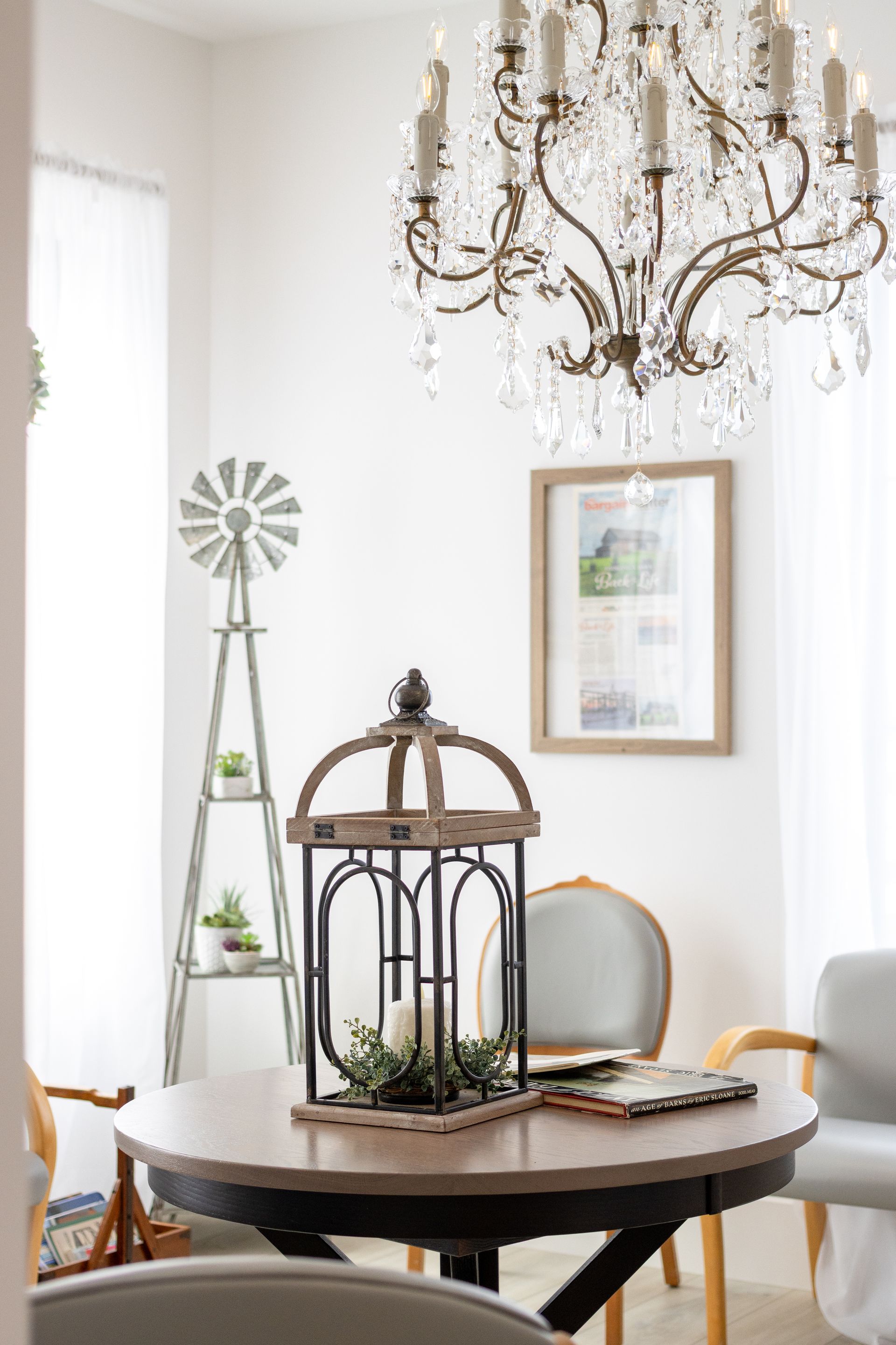 Elegant white living room with a round table, decorative birdcage, chandelier, and framed art.
