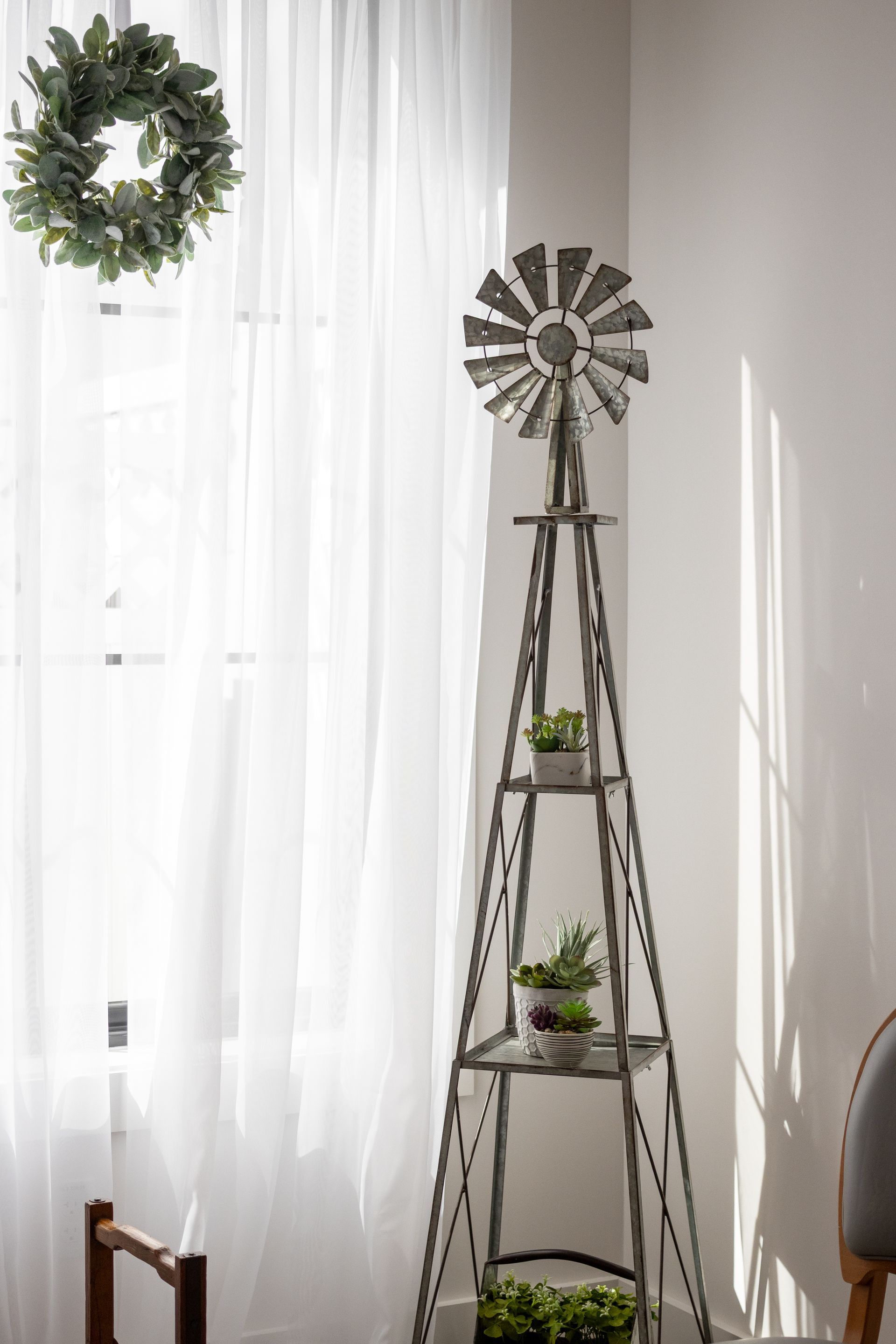 White room with sheer curtains, windmill decor, and a tall metal plant shelf with small potted plants