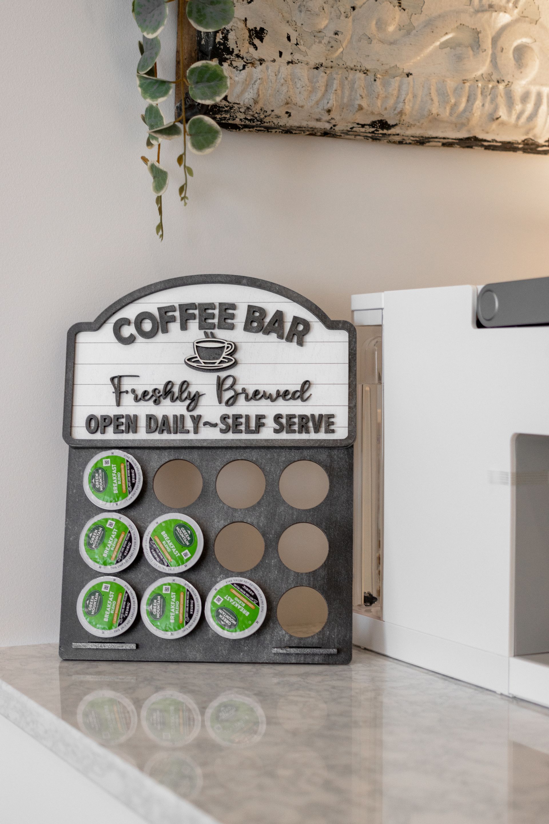 Coffee bar sign with reusable cup markers beside a white appliance on a countertop