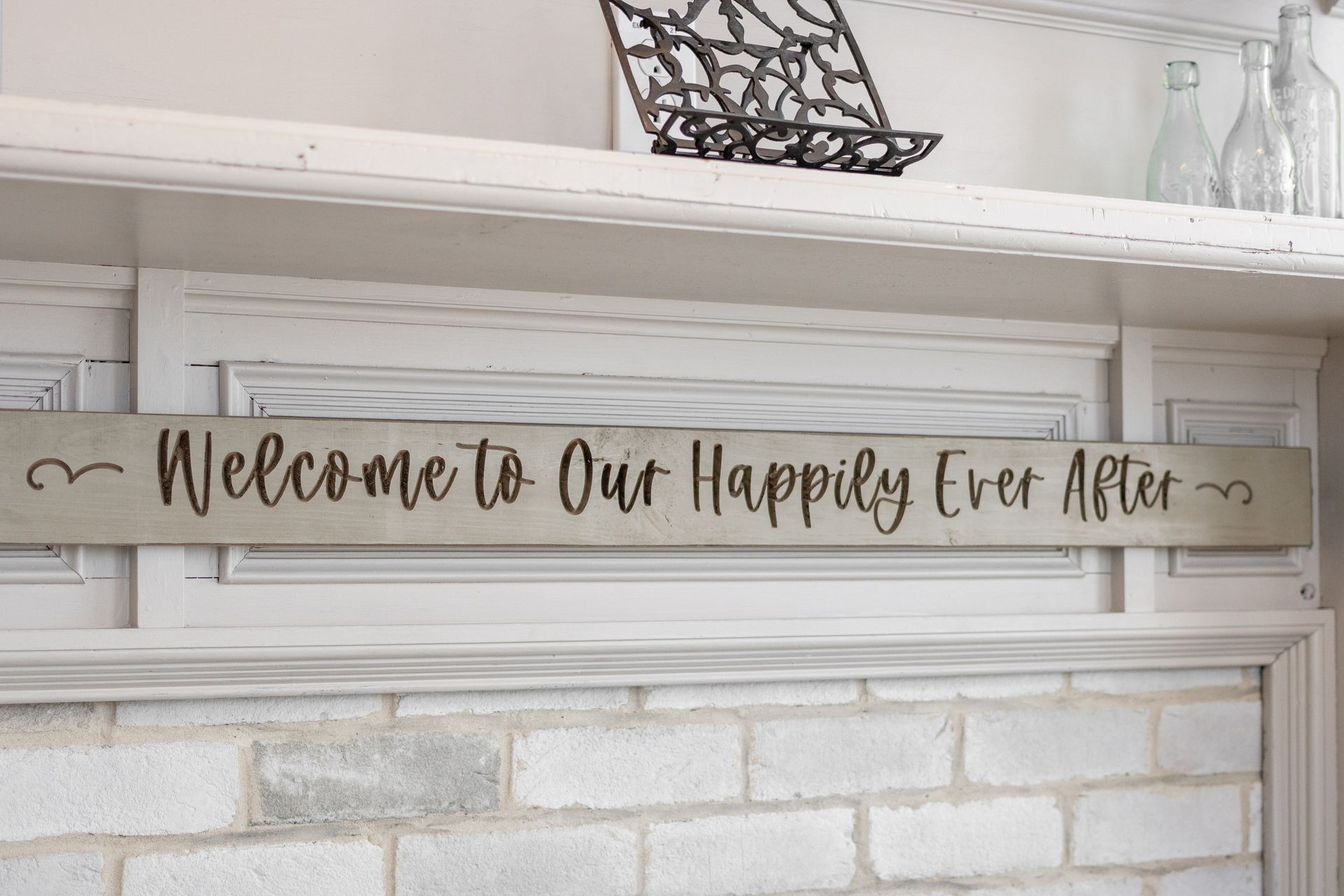Wooden “Welcome to our happily ever after” sign above a white brick fireplace mantel
