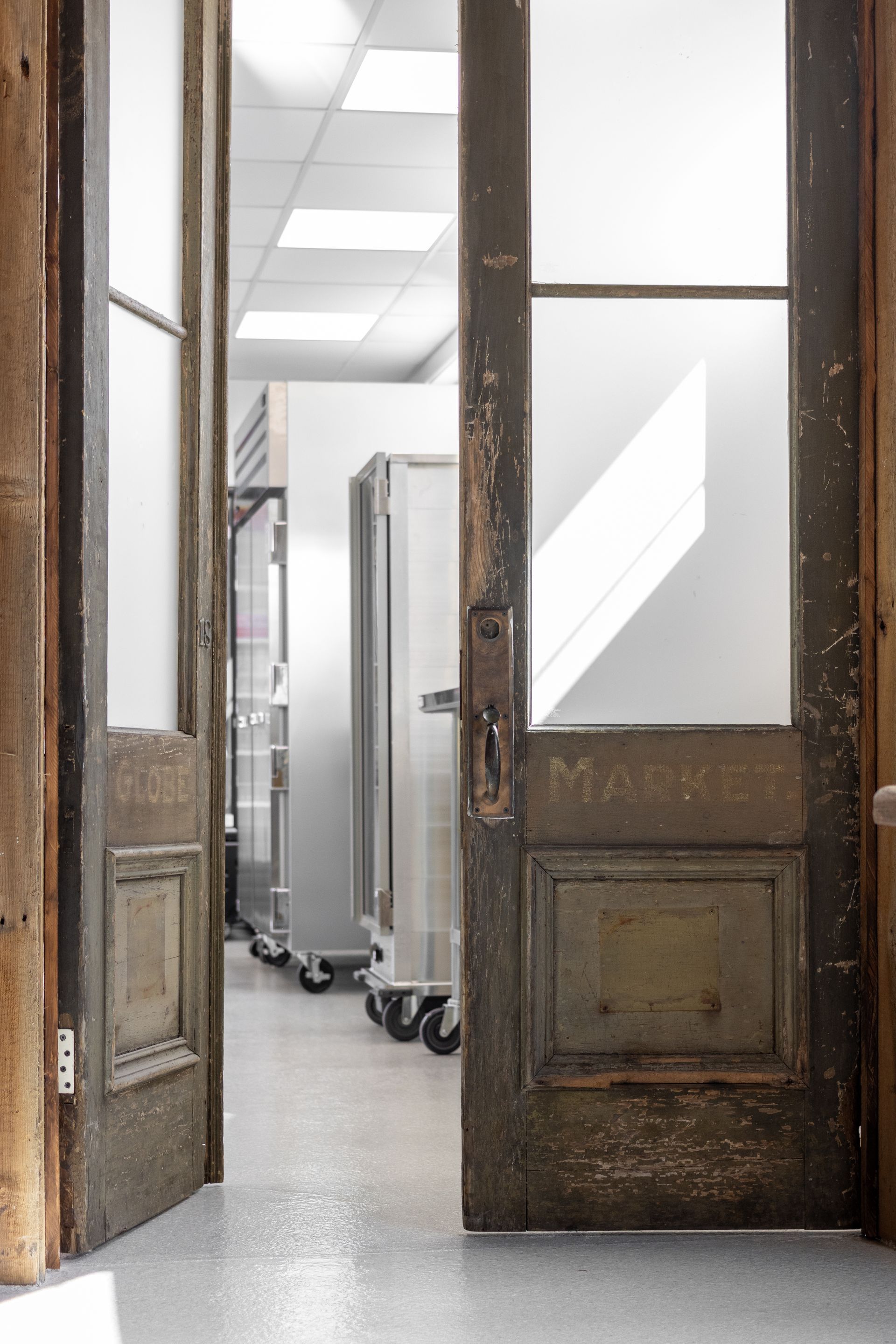 Open wooden doors framing a bright hallway with stainless steel carts and overhead lights