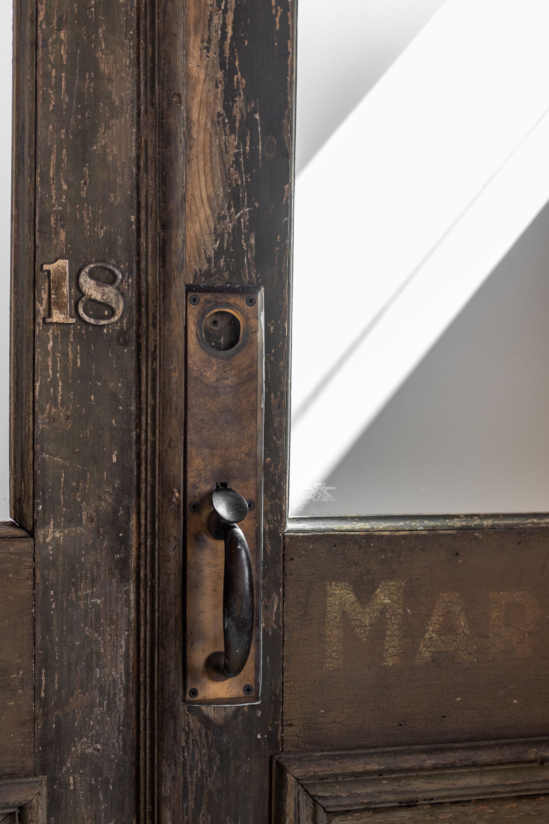 Close-up of a weathered wooden door with metal handle and partial glass panel.