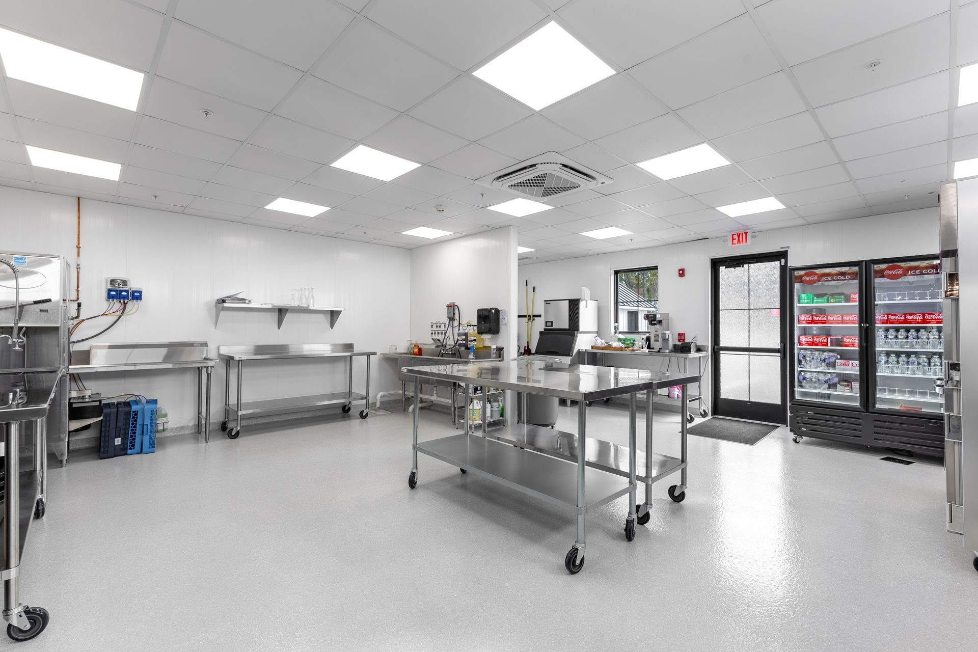 Bright kitchen with stainless steel tables, equipment, shelves, and refrigerators under white ceiling lights