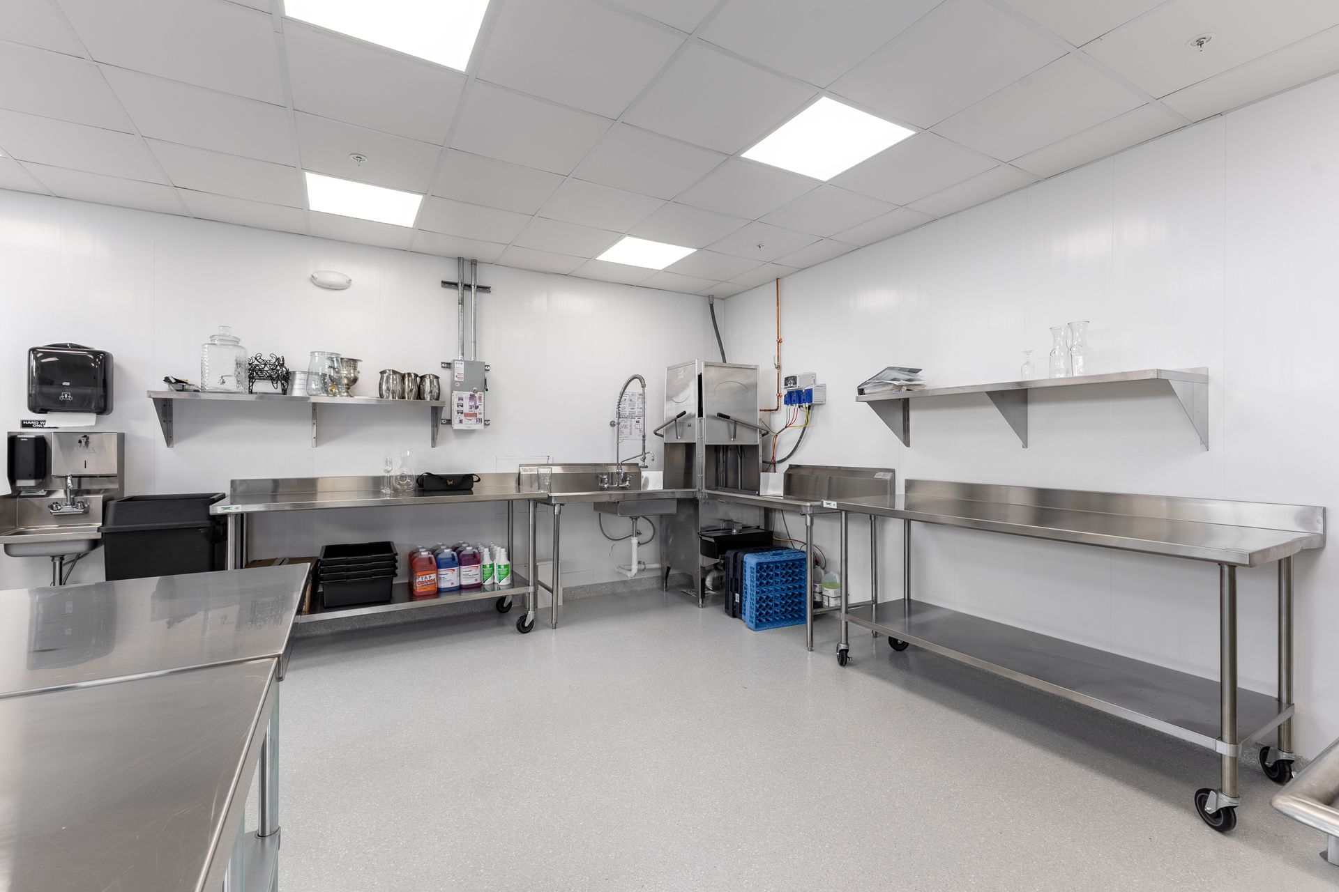 Stainless-steel prep kitchen with counters, shelves, appliances, and bright white tile ceiling