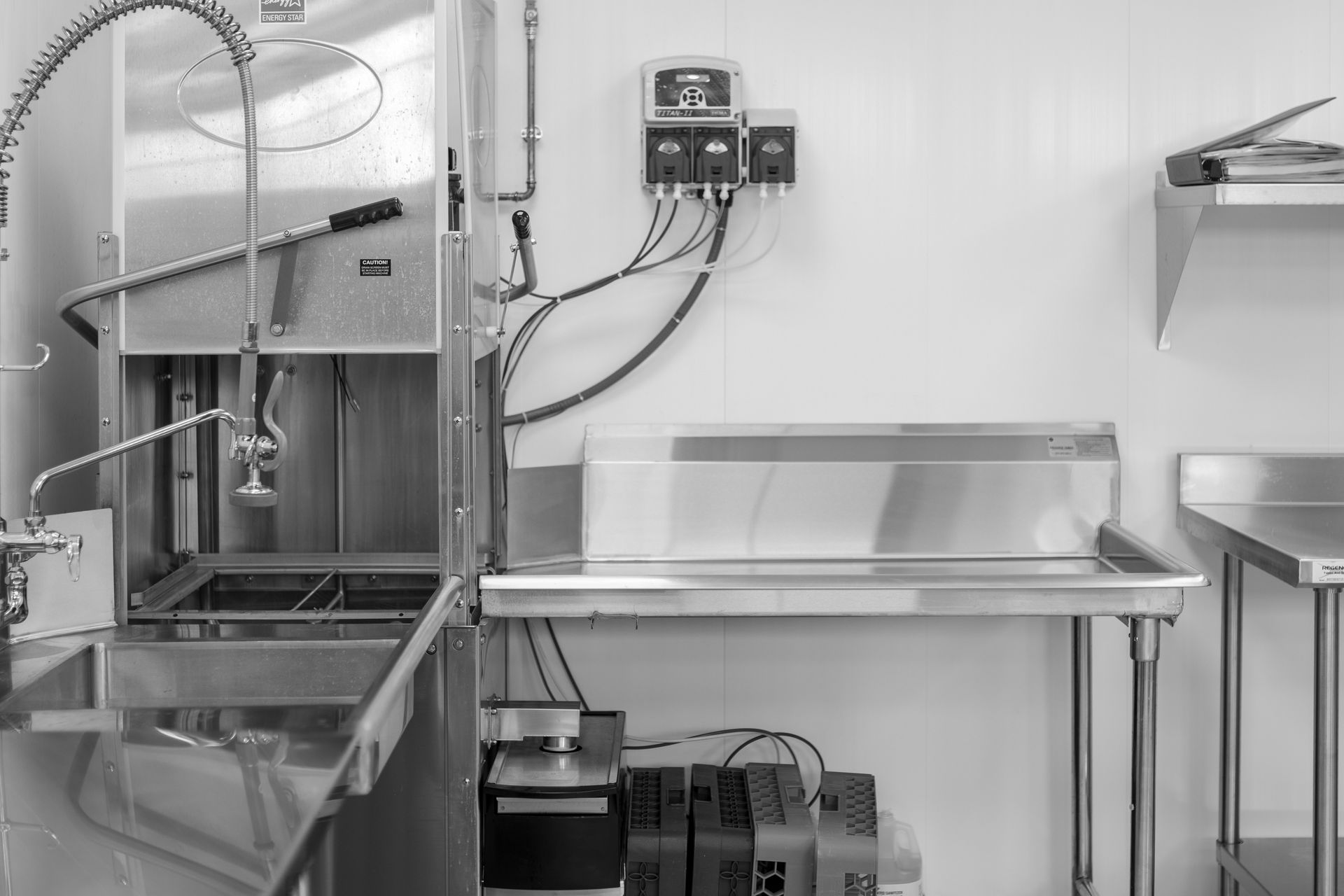 Stainless steel kitchen with shelves, tanks, and a sink under bright overhead lights