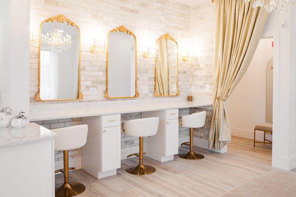 Bridal Suite  interior with gold-framed mirrors, white chairs, brick wall, and draped curtain.