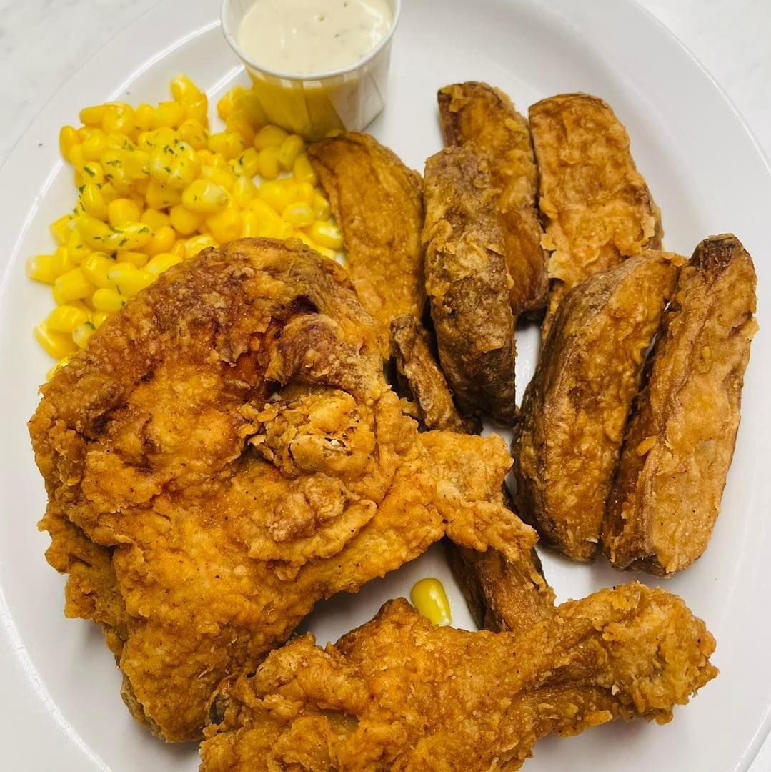 Fried chicken with corn and a small cup of dipping sauce on a white plate