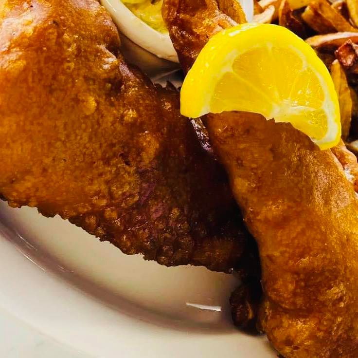 Golden-fried fish fillets with a lemon wedge on a white plate