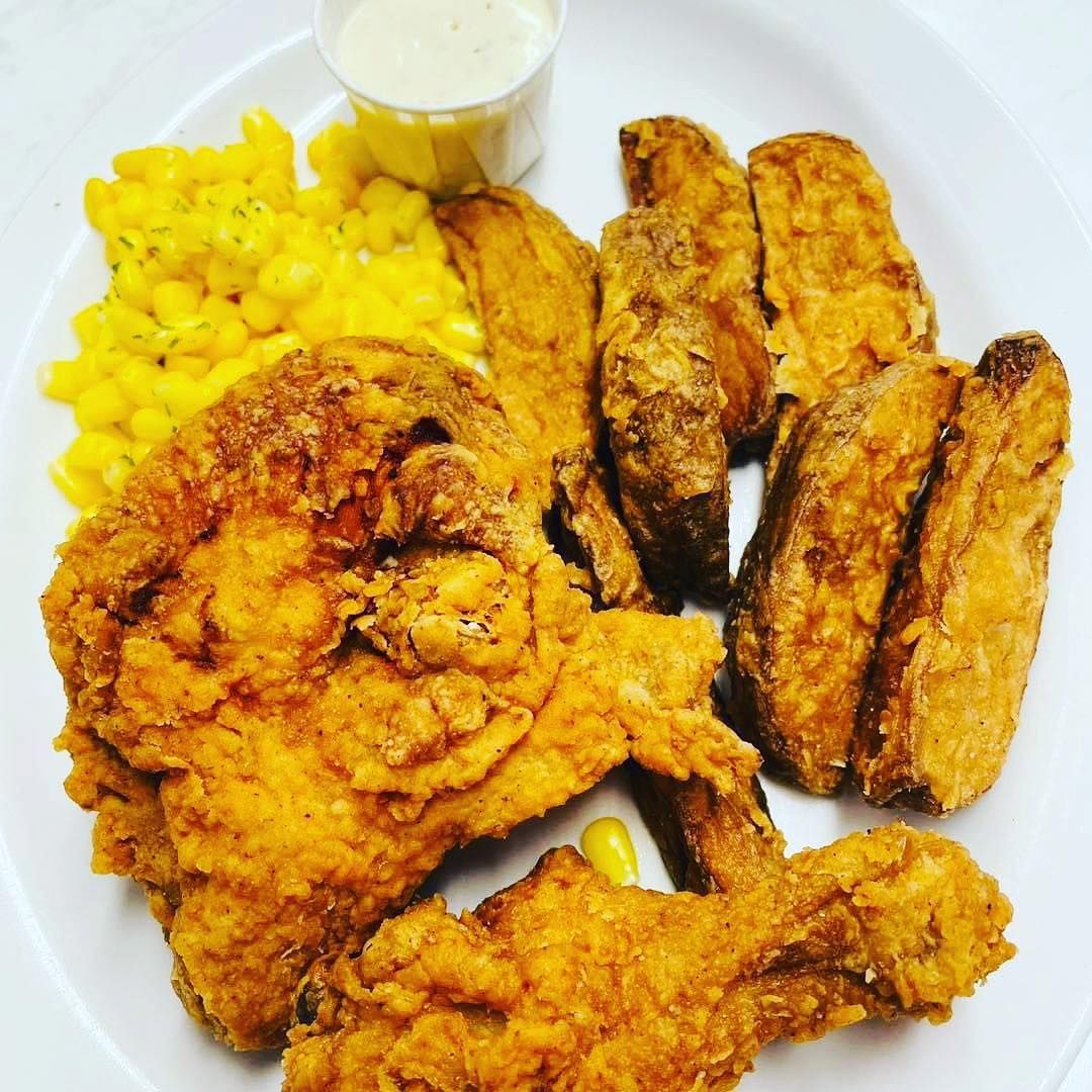 Fried chicken and plantains with corn and a small cup of dipping sauce on a white plate