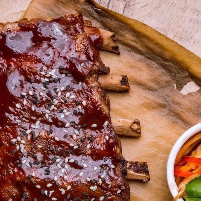 Barbecue ribs glazed with sauce and sesame seeds on a wooden board, with a side of pickled vegetables