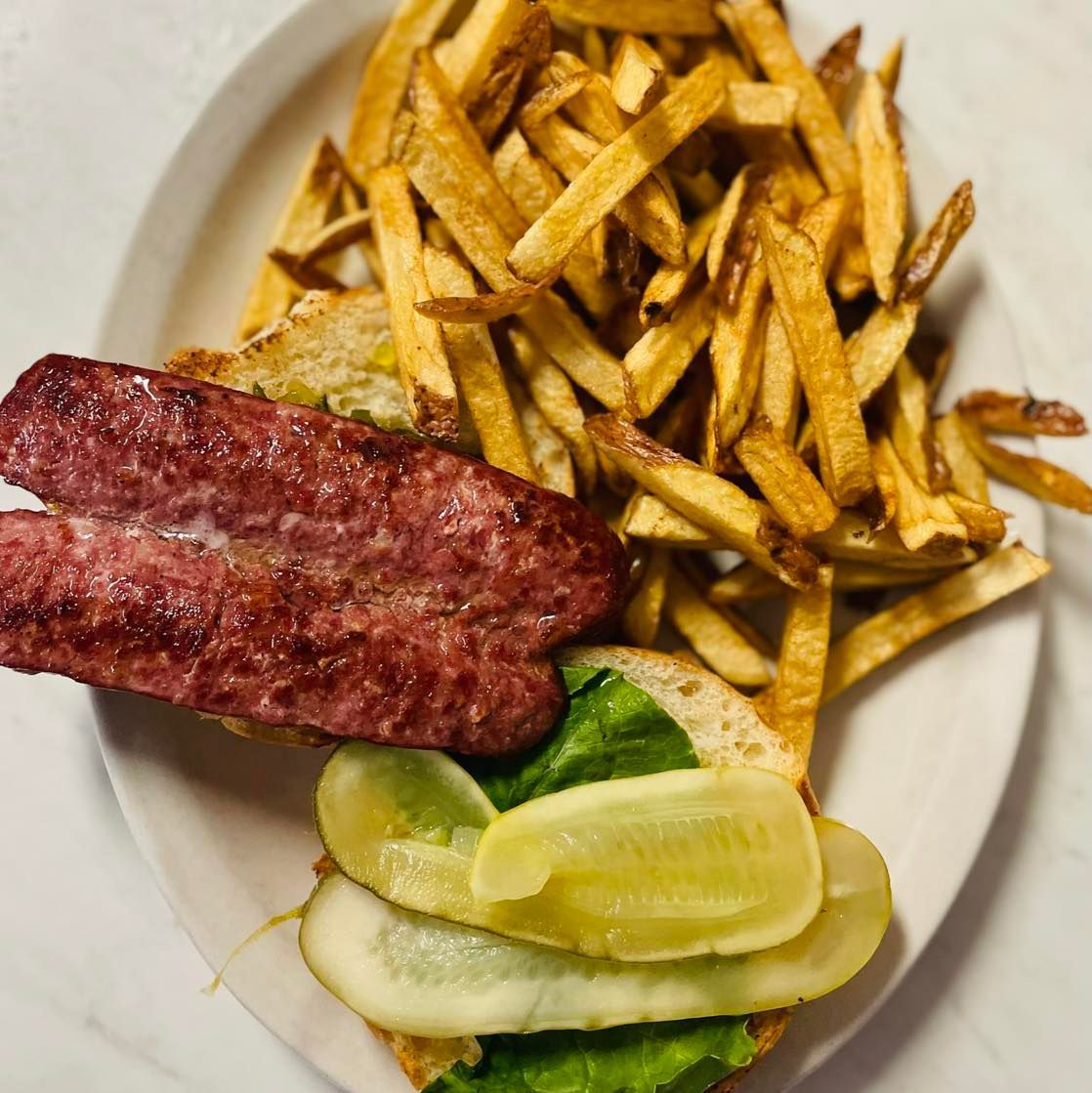 Plate of grilled sausage, French fries, and pickles with lemon wedges